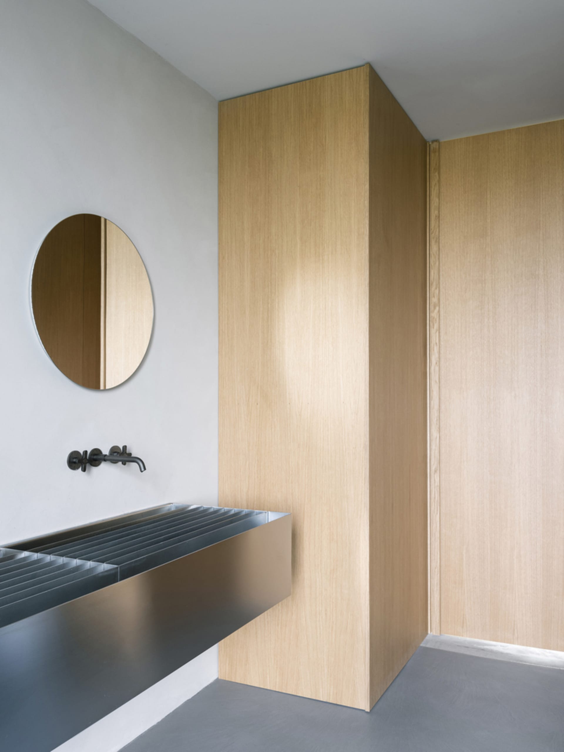 Modern minimalist bathroom with wooden walls and a circular mirror.