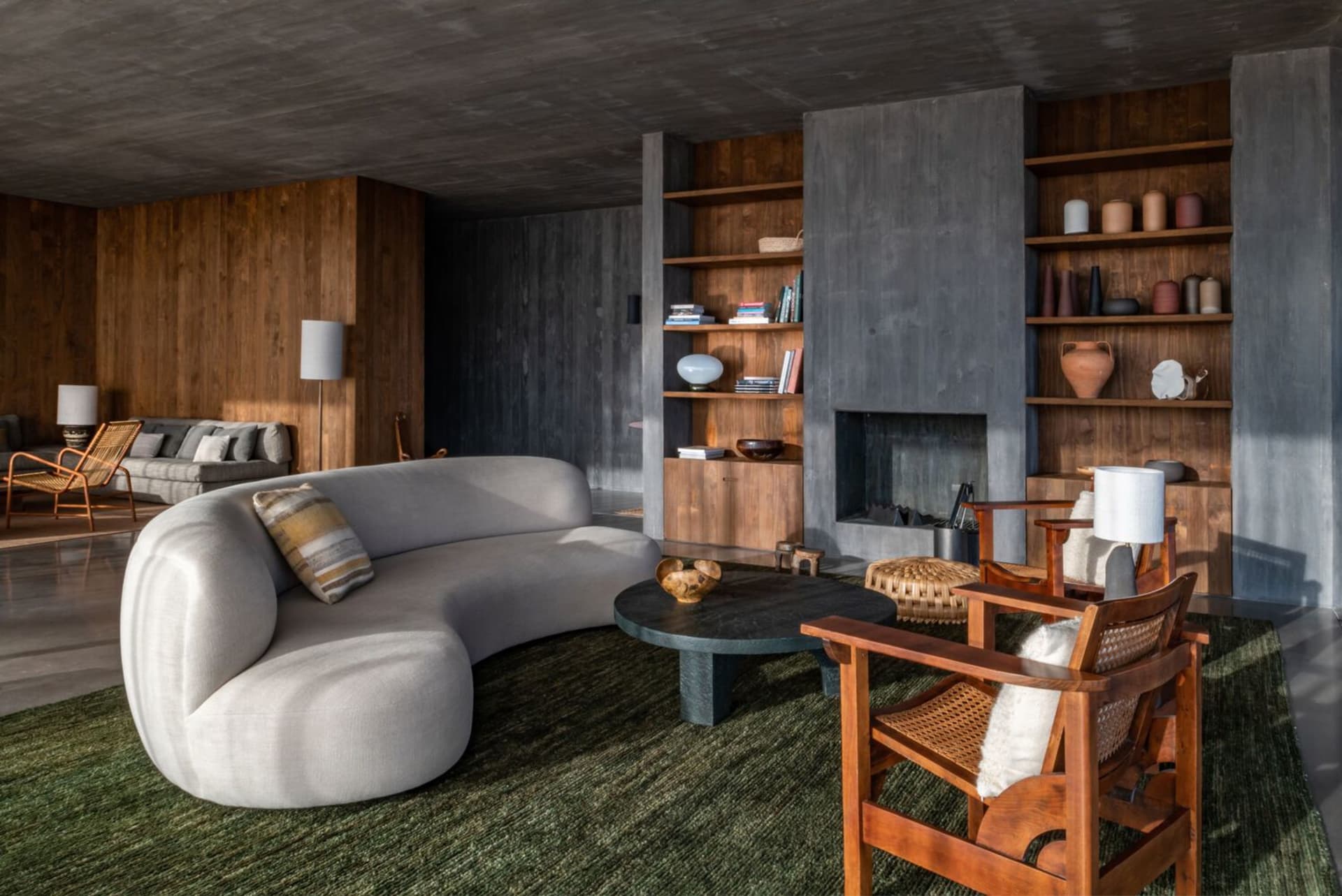 A modern industrial living room featuring a concrete fireplace, wooden shelves, and metal furniture.