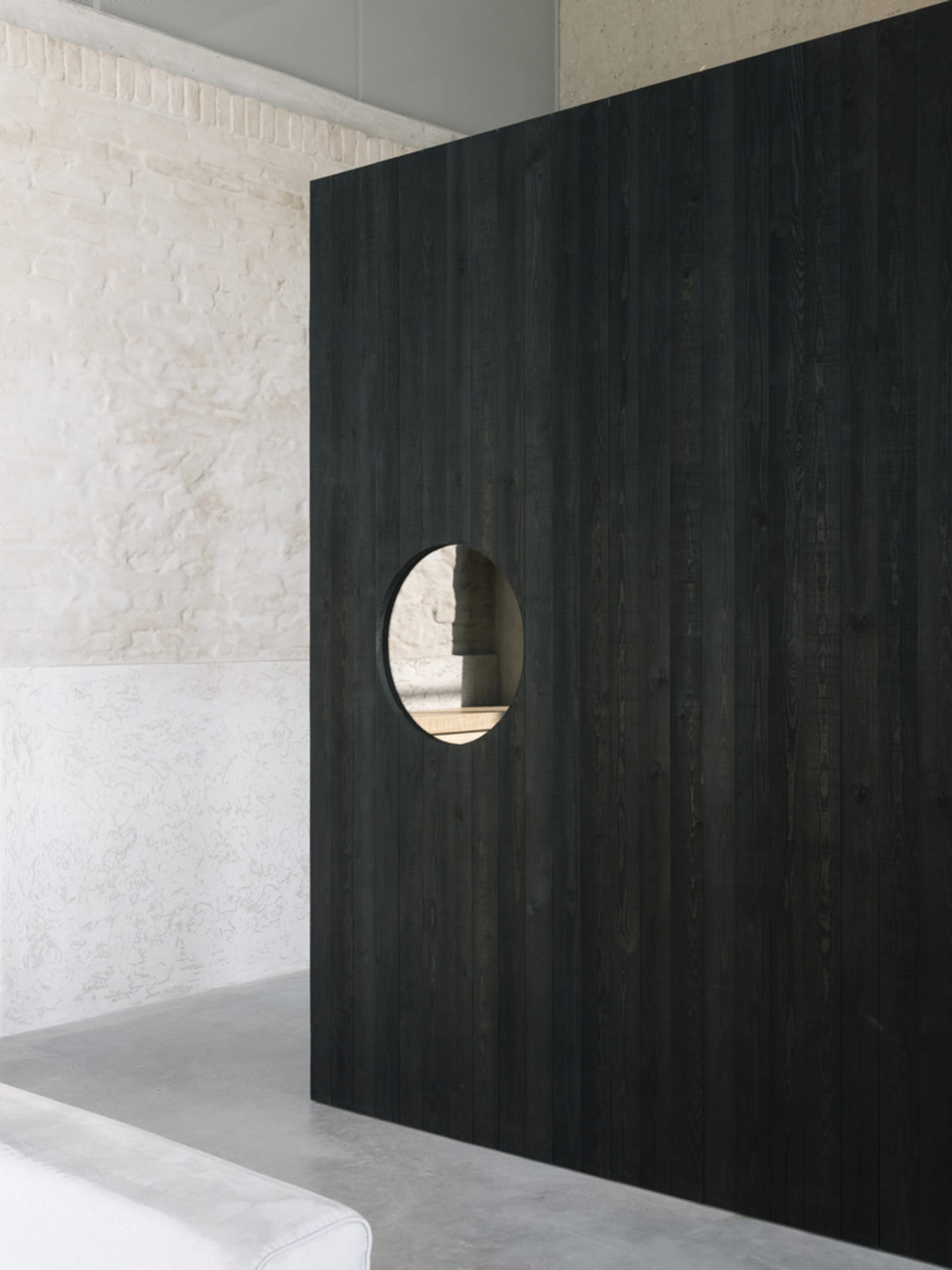 A minimalist interior design with a dark wooden wall featuring a circular cutout.