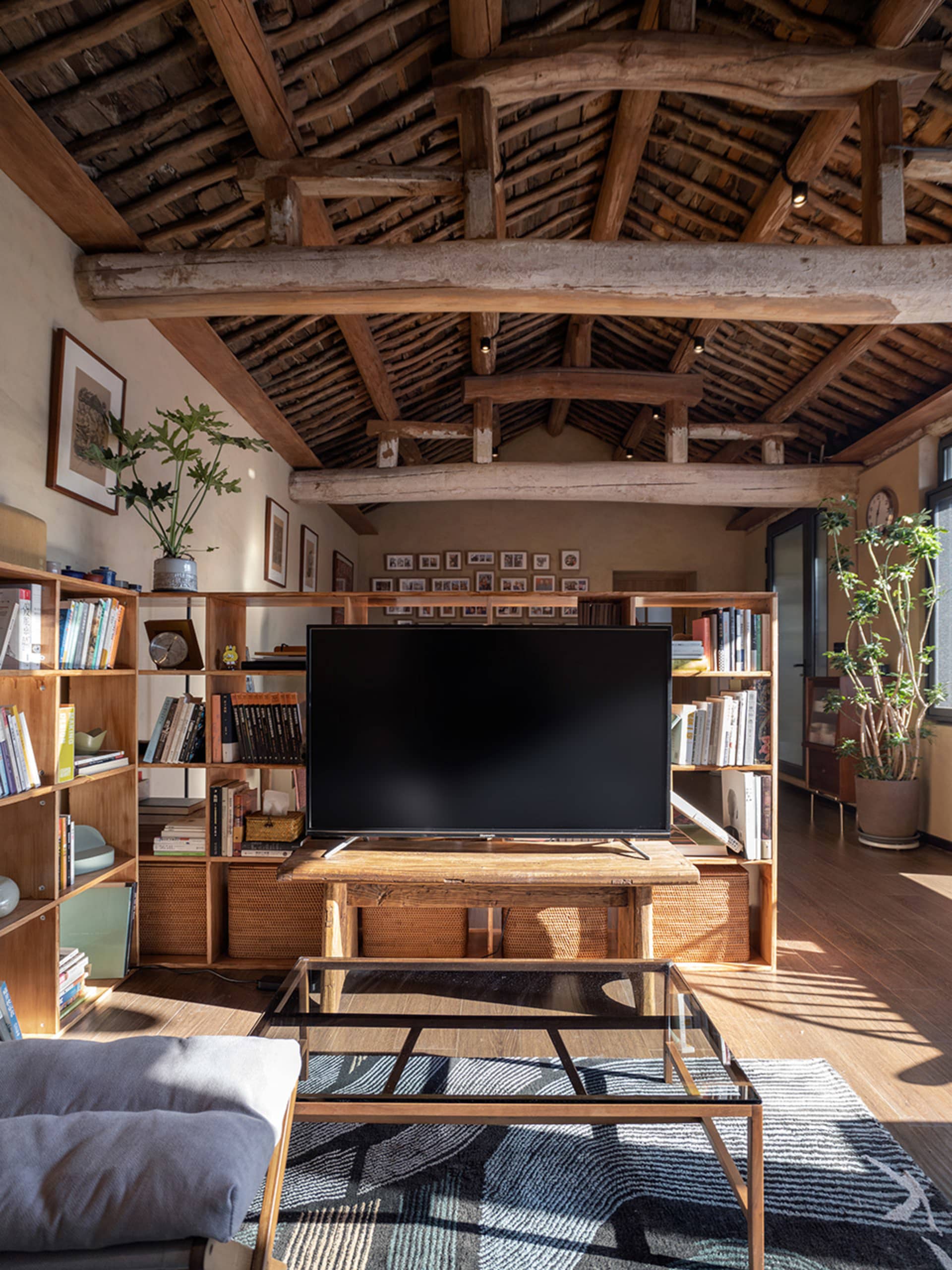 A minimalist living room with wooden furniture, plants, and a flat-screen television on a wooden table.