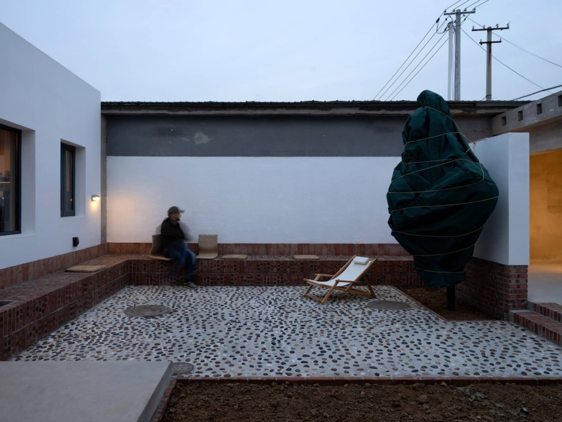 A modern exterior residential space featuring a rendered concrete patio and seating area with a person sitting on a bench.