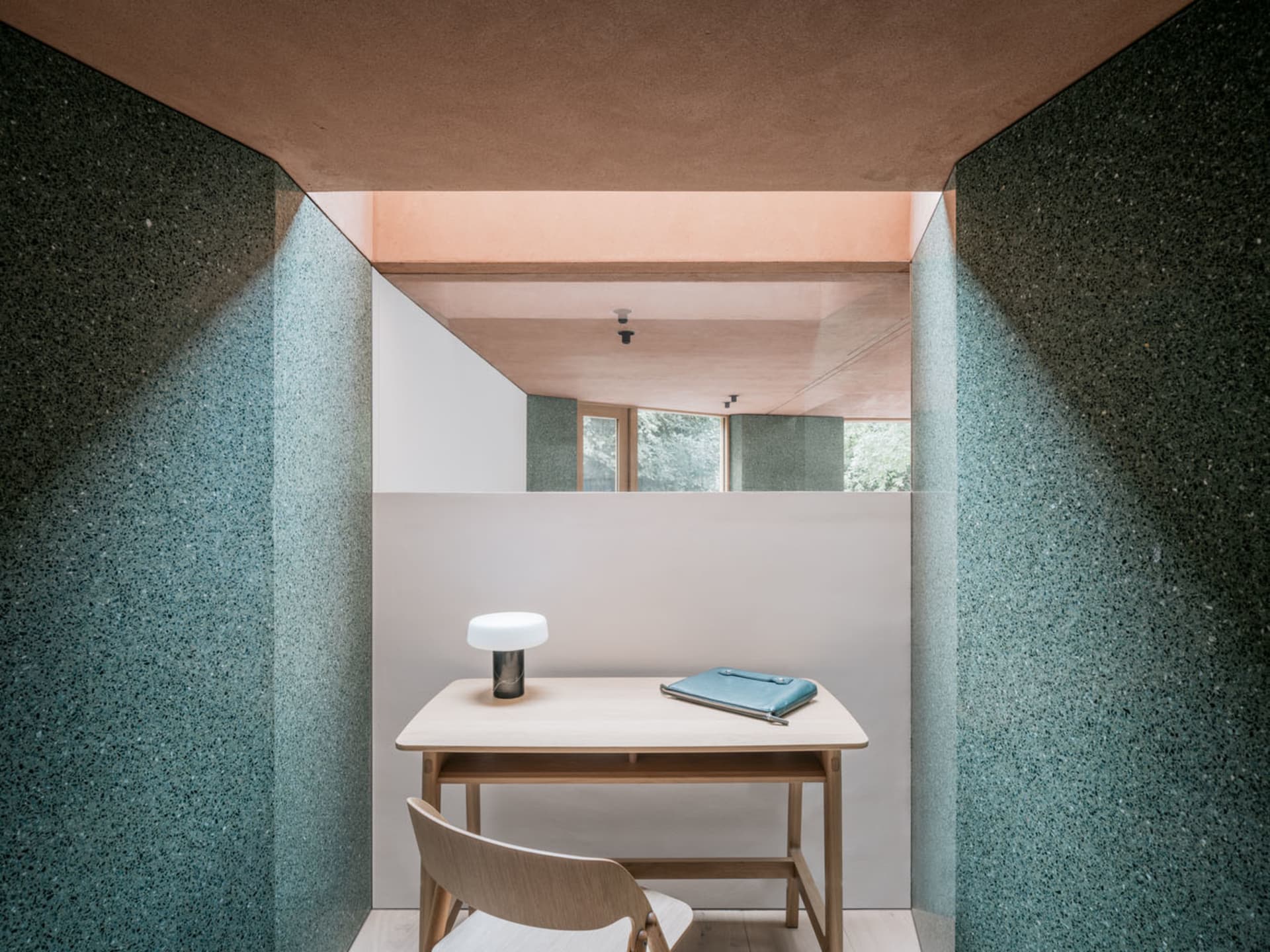 A minimalist office space featuring a desk, chair, and lamp with a concrete wall and floor.