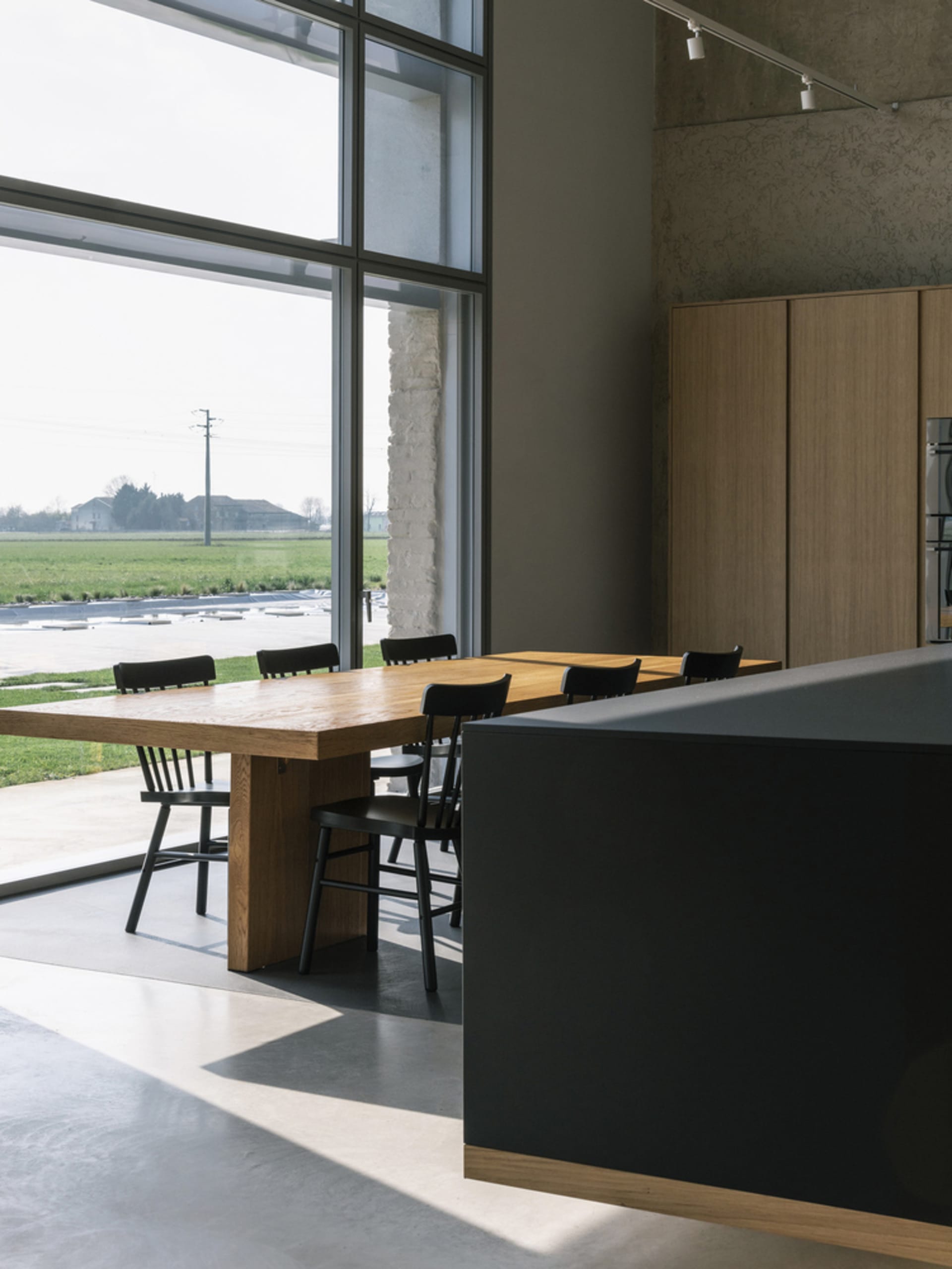 Modern dining room with wooden furniture and large windows overlooking green fields.