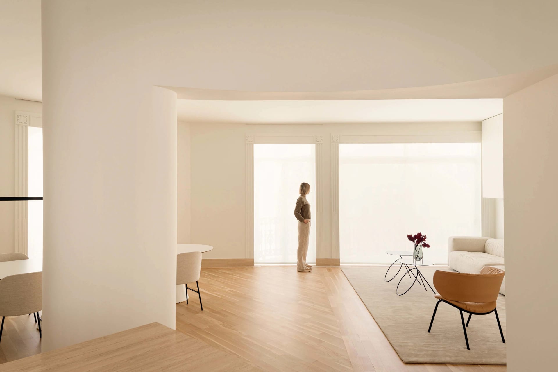 A modern minimalist lounge area with neutral tones, featuring a white sofa, wooden floor, and large windows.