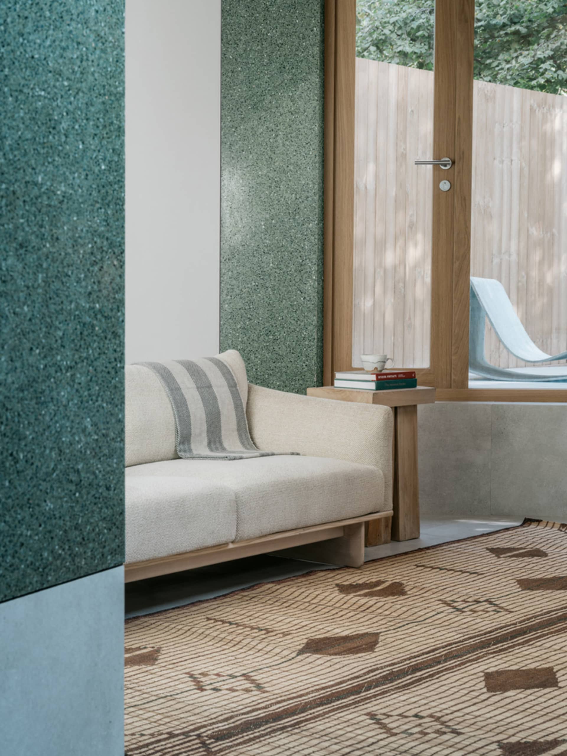 A modern living room with concrete walls and a large window overlooking a natural outdoor area.