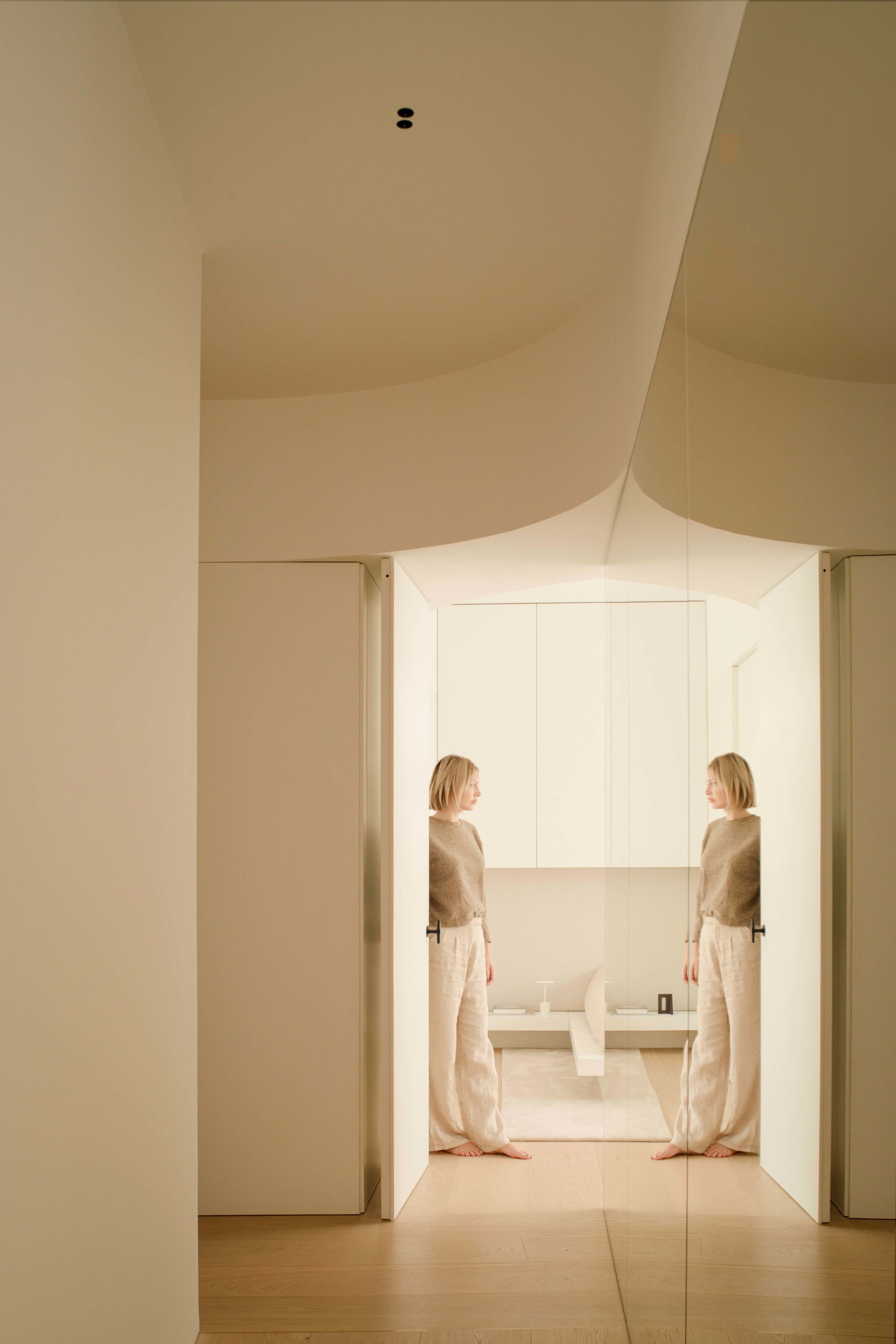 A woman standing in a minimalist residential space with beige walls and flooring, featuring geometric forms and natural light