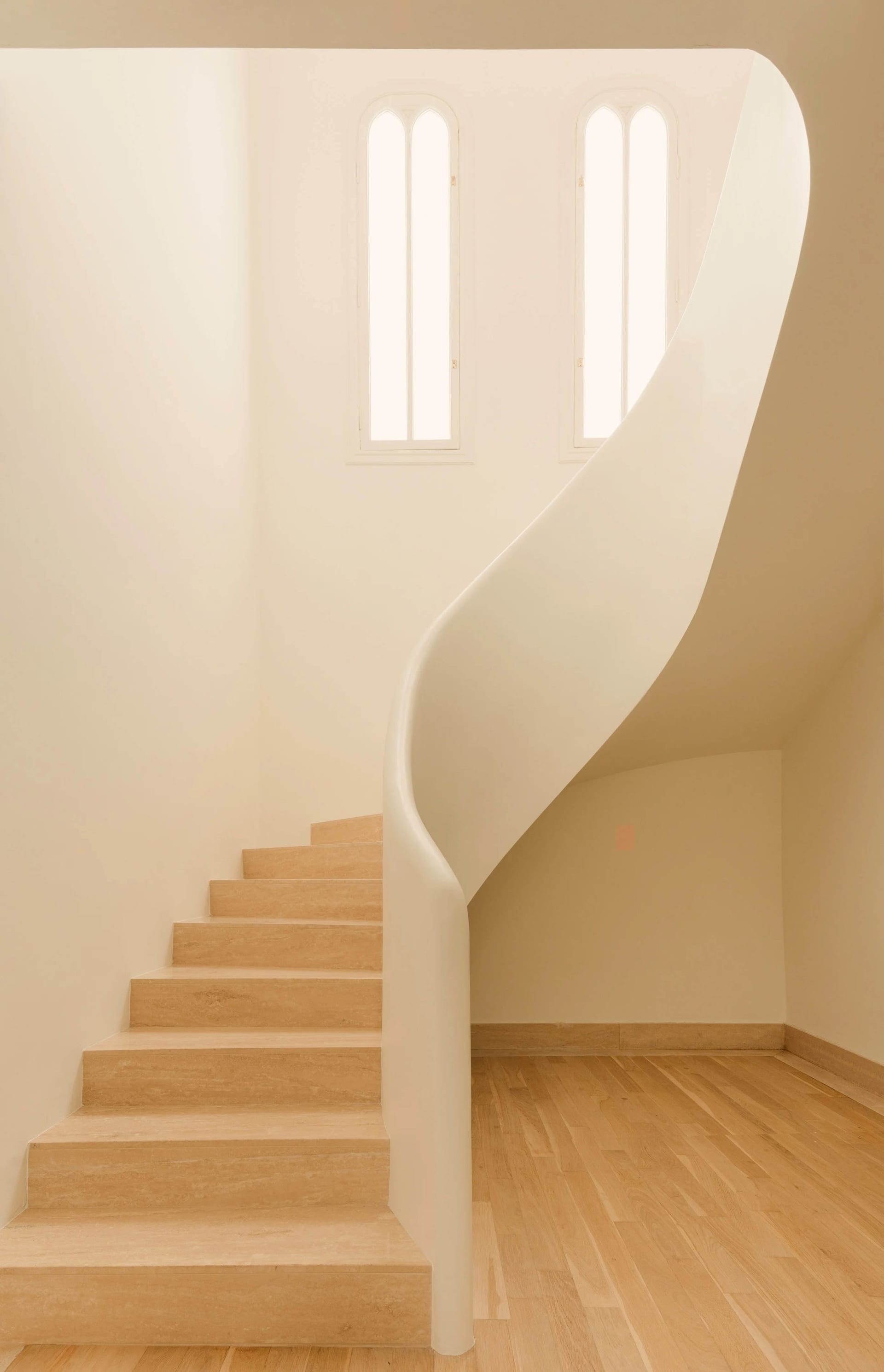 A modern interior staircase with wooden steps and railings, featuring an archway and natural light.