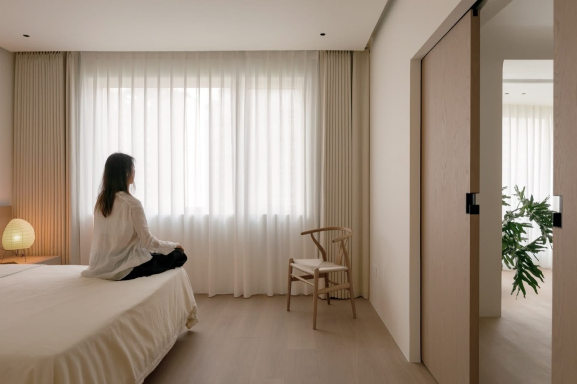 簡約臥室內有白色床鋪、木地板,以及大窗旁的白窗簾。