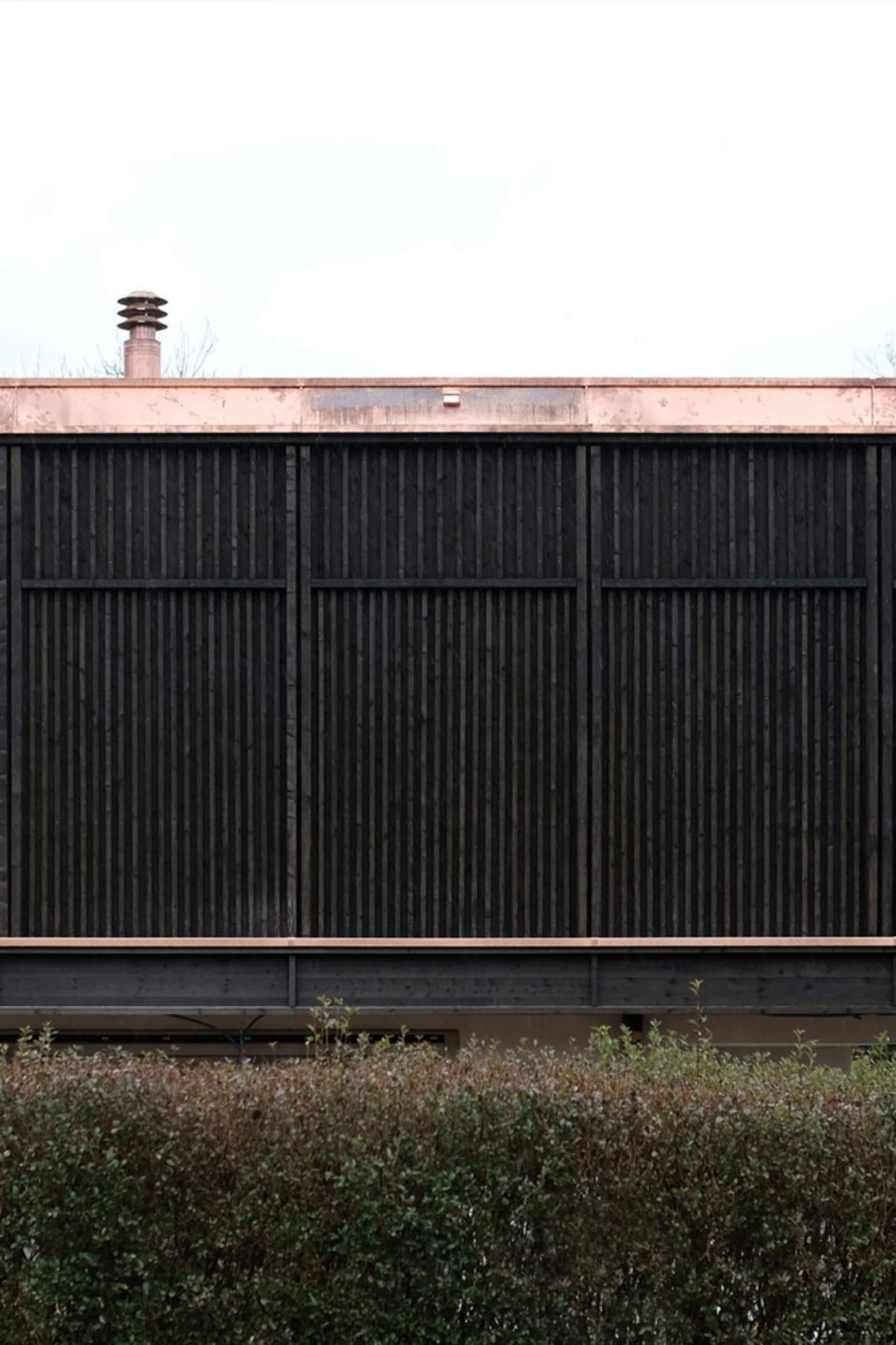 A modern arbor with a dark wooden slat design and a copper roof.