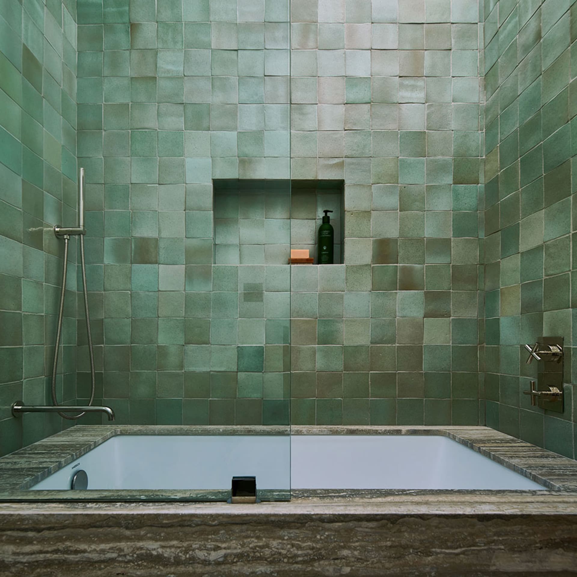A modern bathroom featuring green square tiles on the walls, a built-in bathtub, and a shower area.