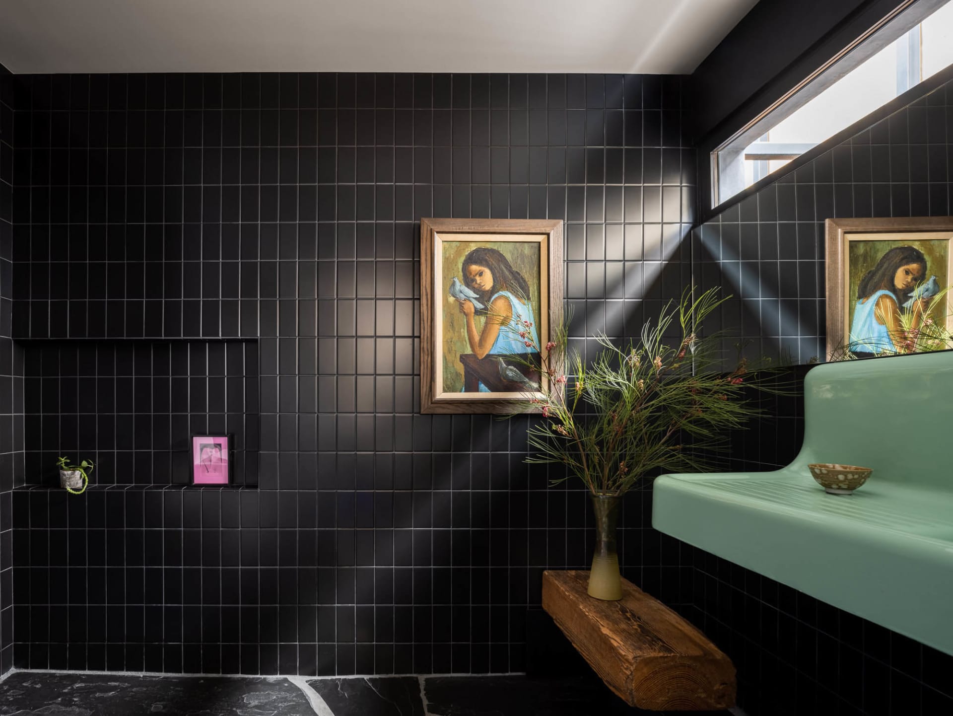 A modern minimalist bathroom with black tiled walls, concrete floor, and green plants