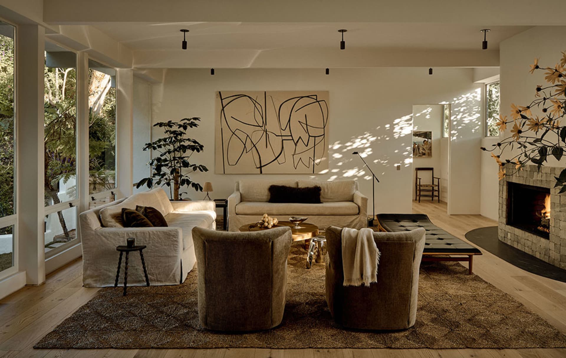 A modern interior living room featuring neutral textiles and earth tones, with a fireplace, sofas, armchairs, and large artwo