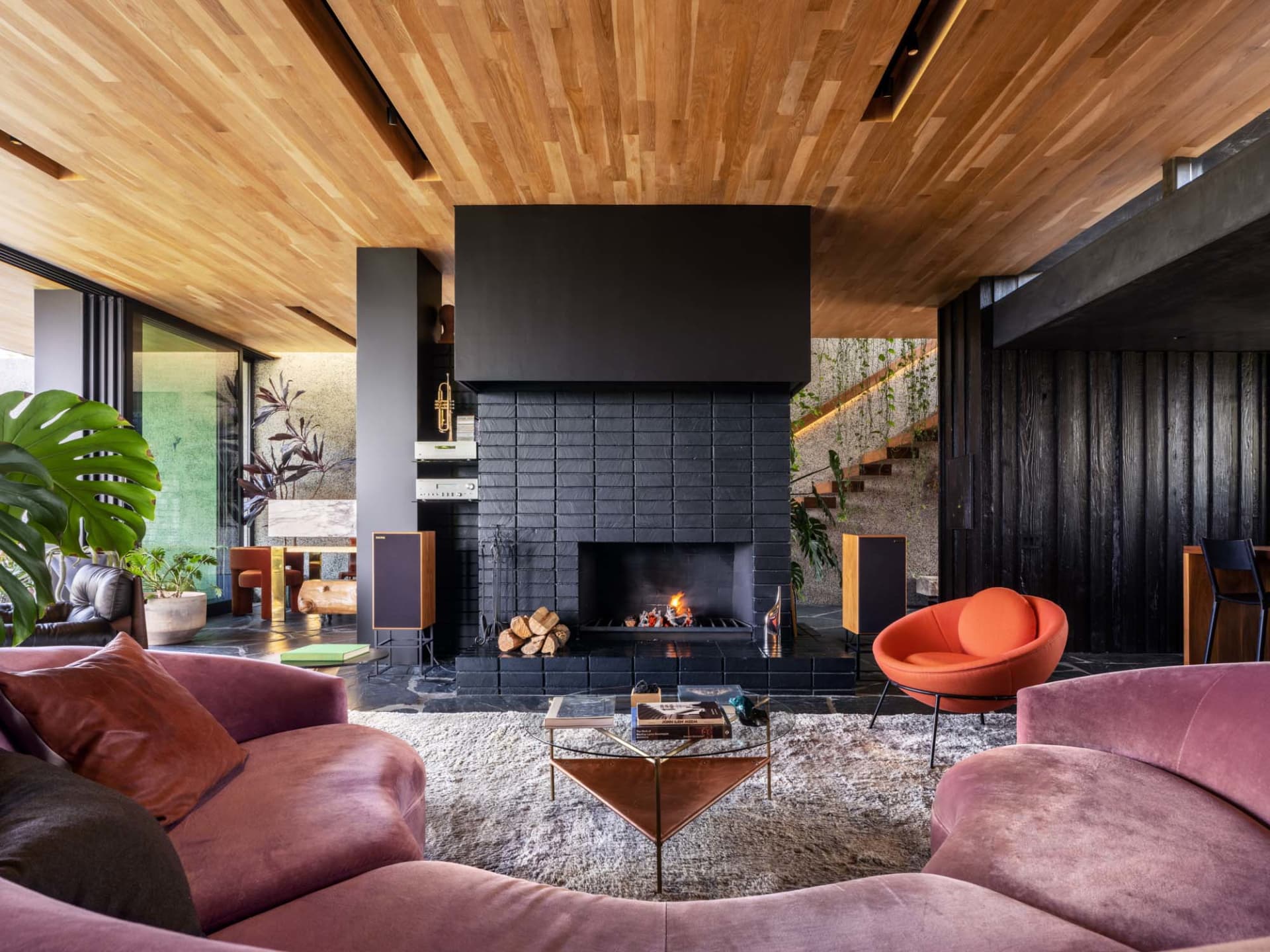 A spacious, industrial-style living room featuring a prominent, modern fireplace made of black slate tiles, surrounded by pin
