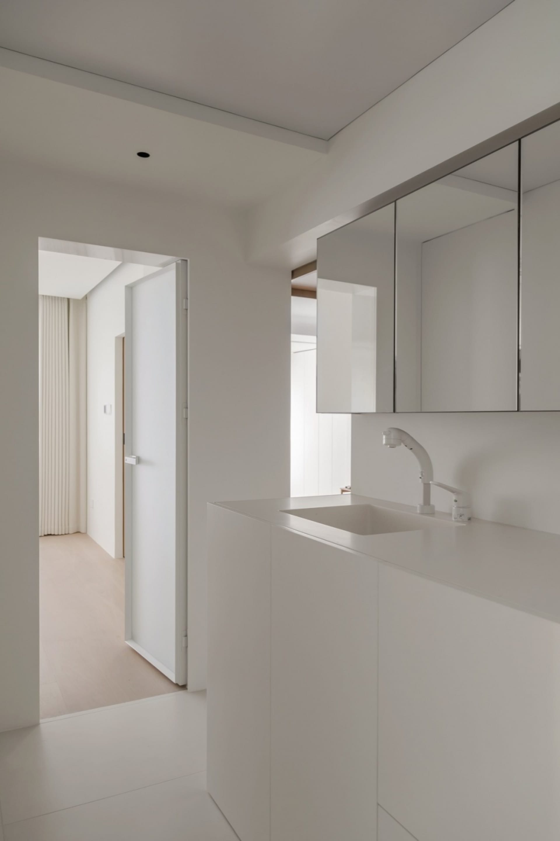 A minimalist white bathroom with a single sink, mirror, and cabinet.