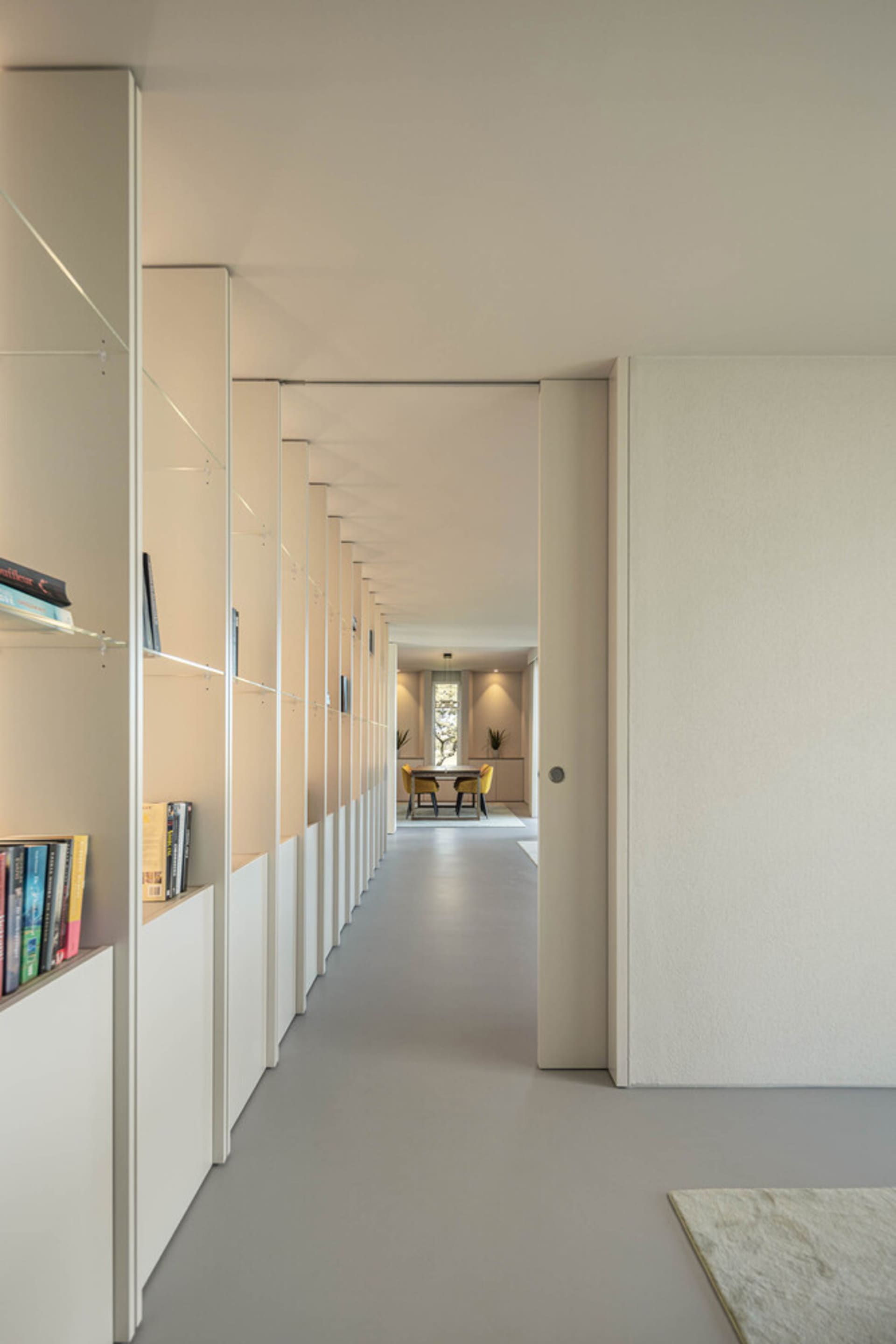 Modern hallway with white walls, glass shelves, and concrete floor