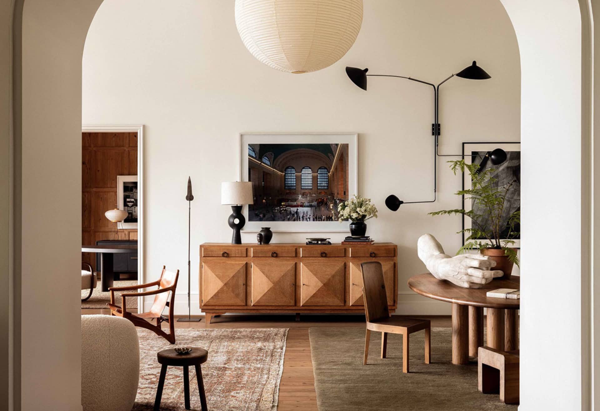 A modern minimalist living room featuring wooden furniture, a round wooden table, and a wooden credenza.