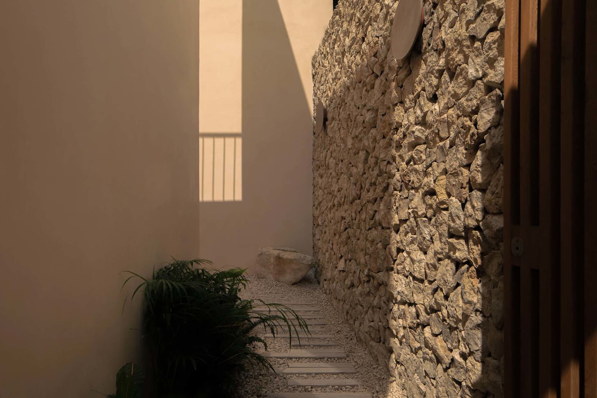 A narrow stone-walled hallway with a plant and sunlight coming through a window.