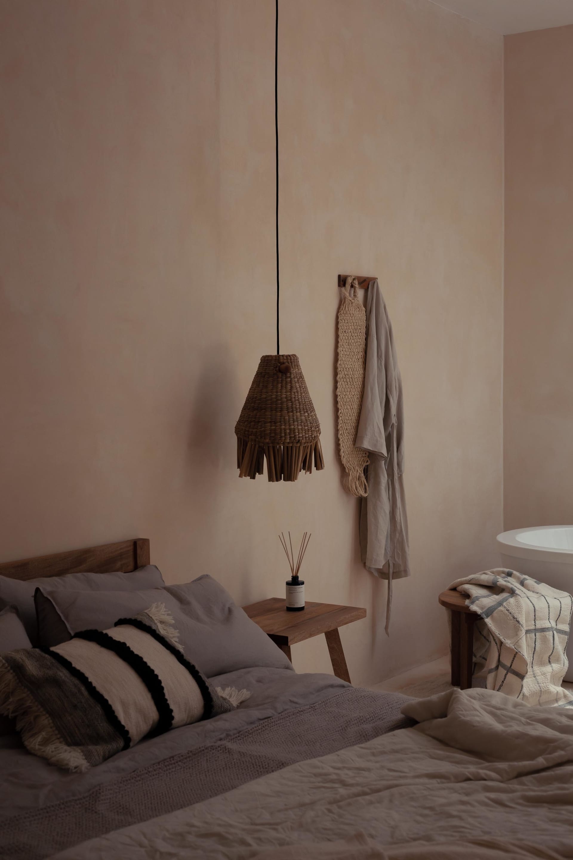 A minimalist bedroom featuring textile accents, wooden elements, and a wicker lampshade.