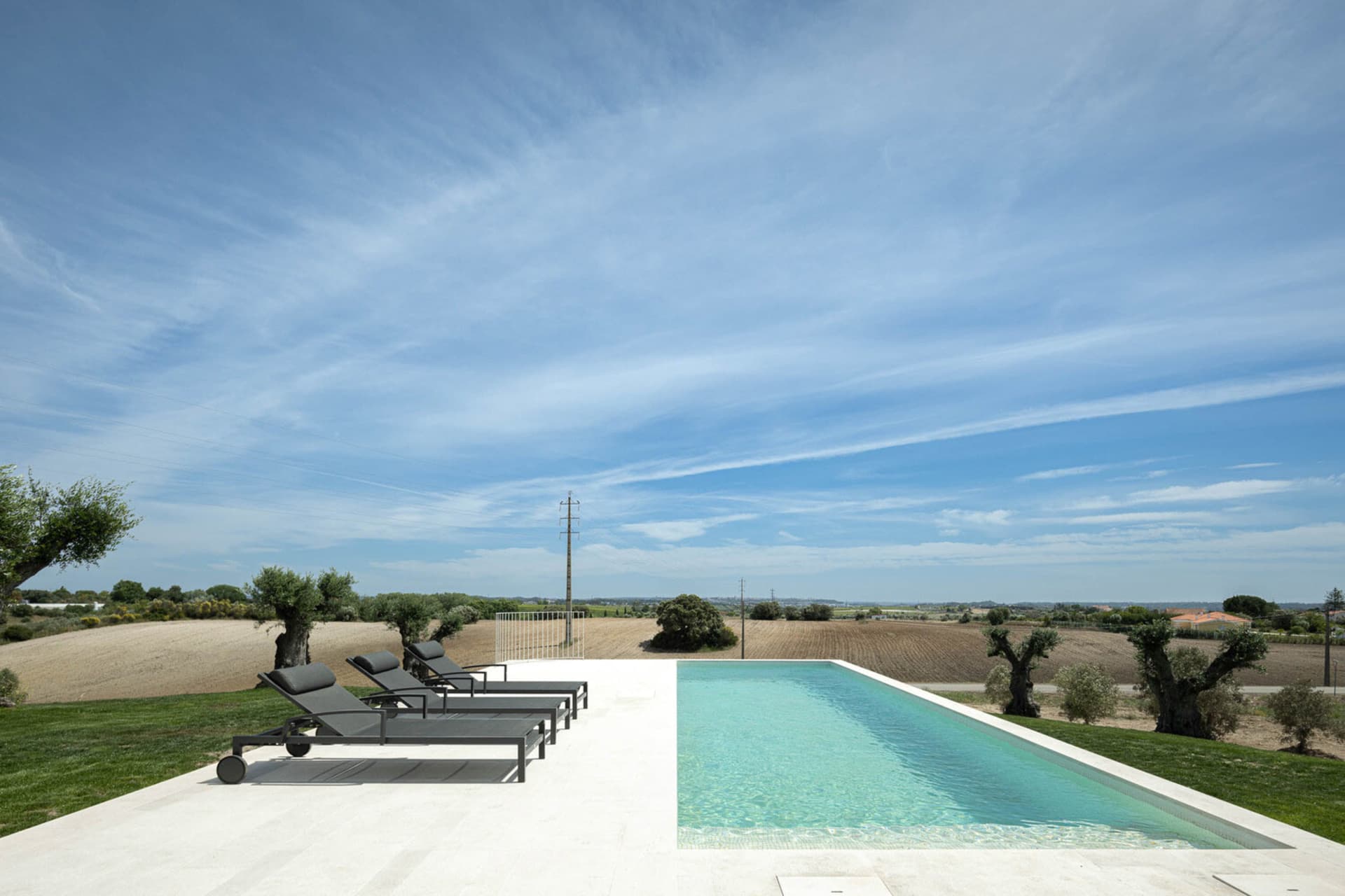 A minimalist villa with a concrete pool overlooking a vast agricultural landscape.