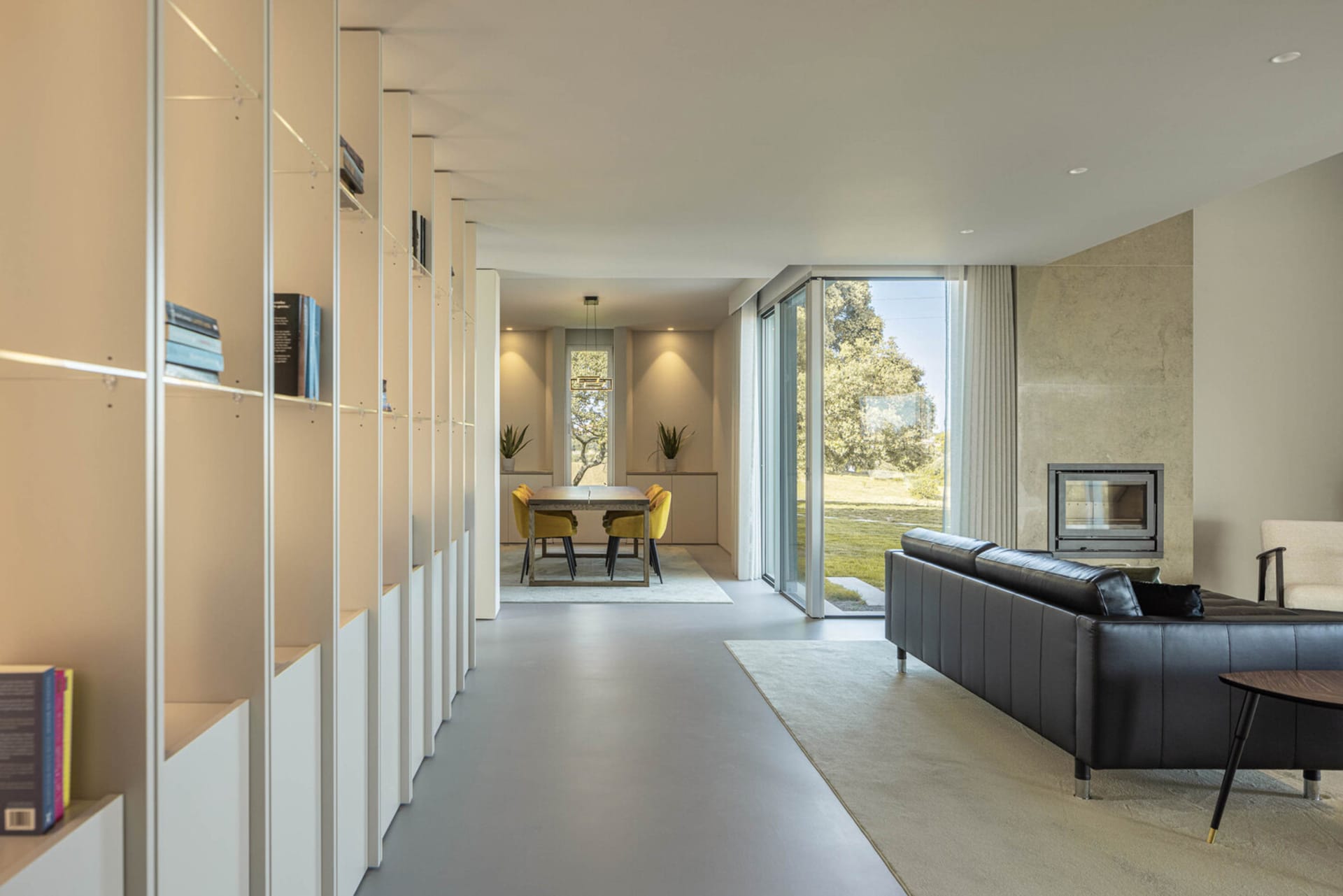 A modern living room with a concrete fireplace and black leather sofas, featuring minimalistic design and natural light.