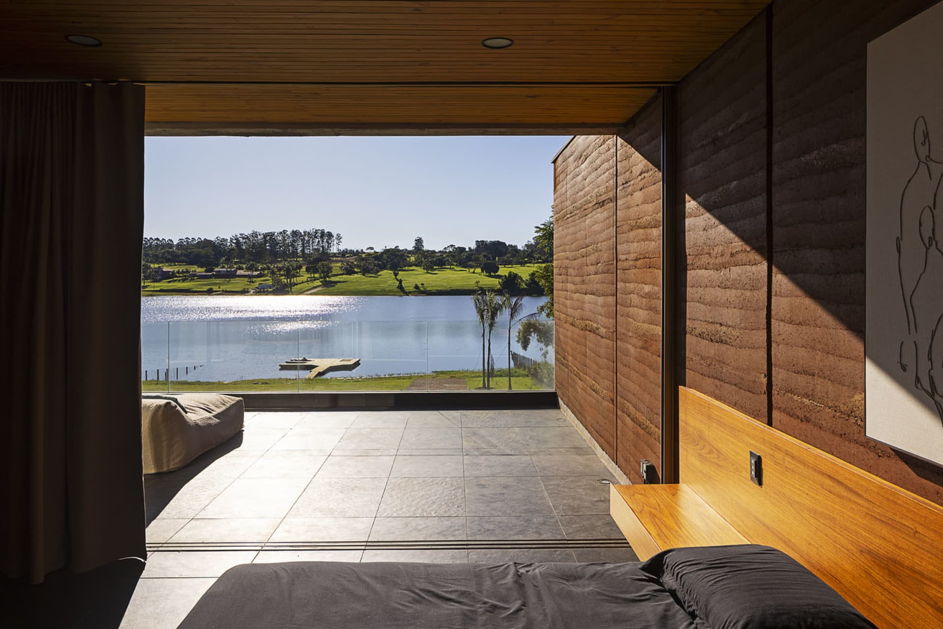 A minimalist bedroom featuring a black bedspread and a wooden headboard, with a view of a lake.