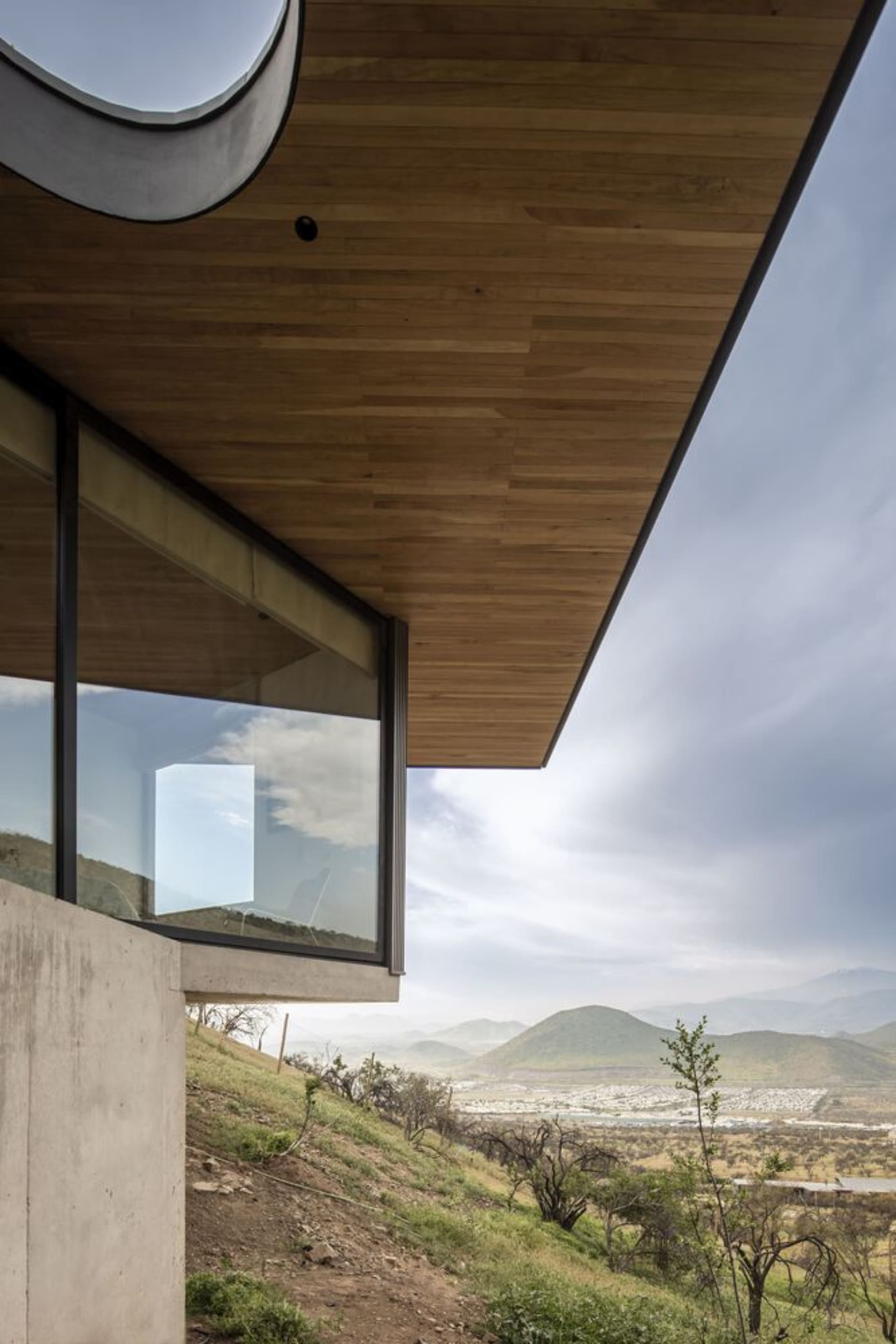 A modern house situated on sloped ground, featuring wood siding, concrete walls, and large glass windows.