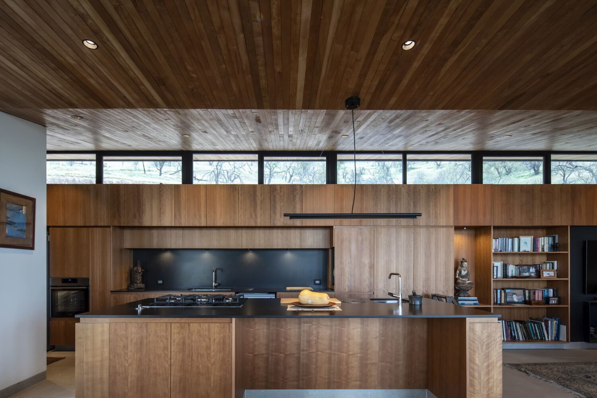 Modern industrial kitchen with wooden furniture and black countertops, featuring a large central island and floor-to-ceiling