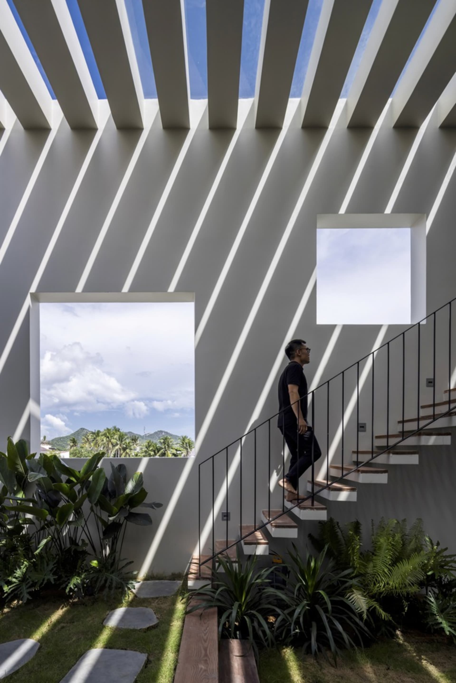 A man is walking up a modern, concrete staircase with large windows and greenery.