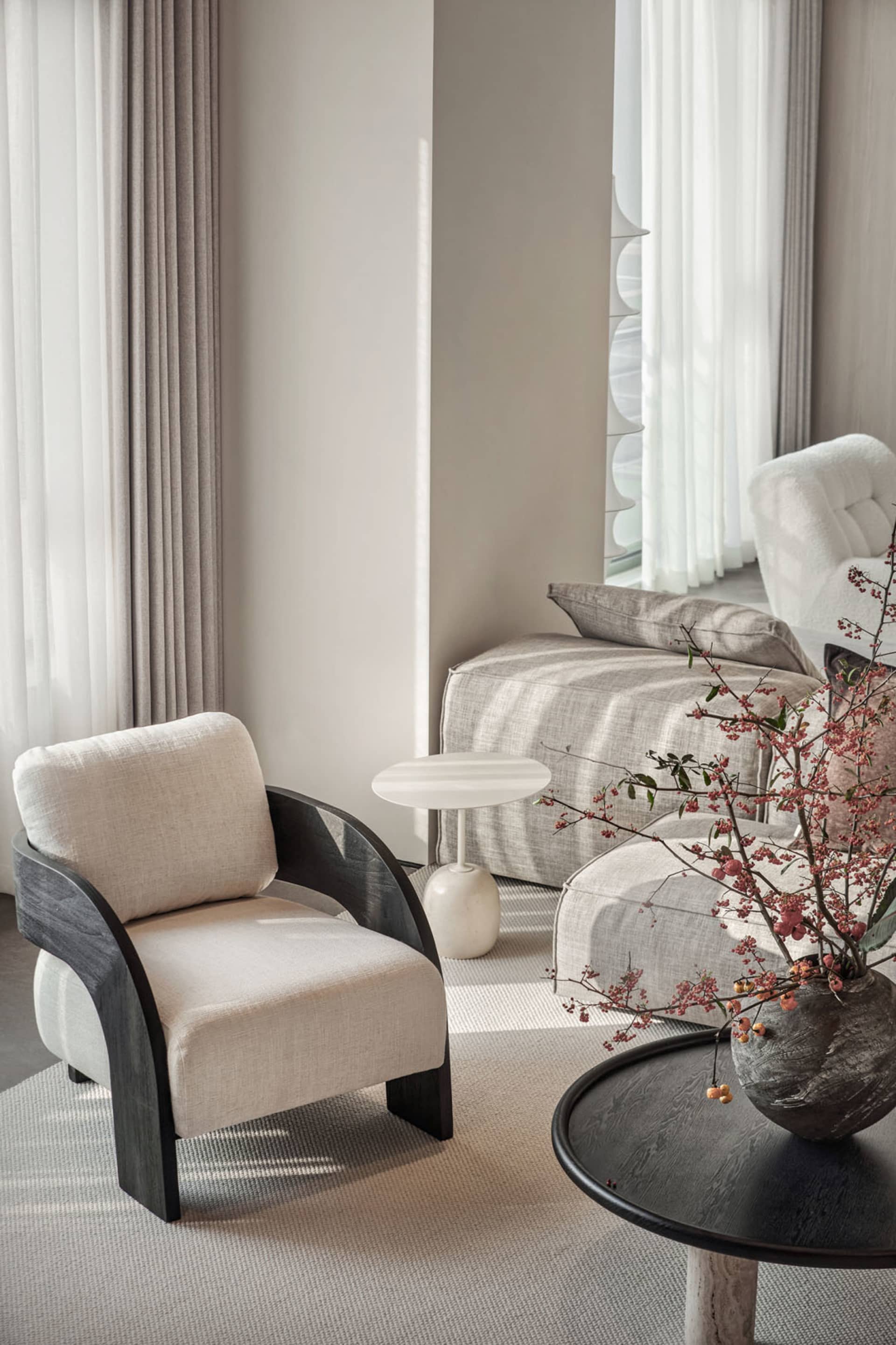 A modern living room with a white fabric armchair, a marble side table, and a wooden coffee table. The room features a sofa w