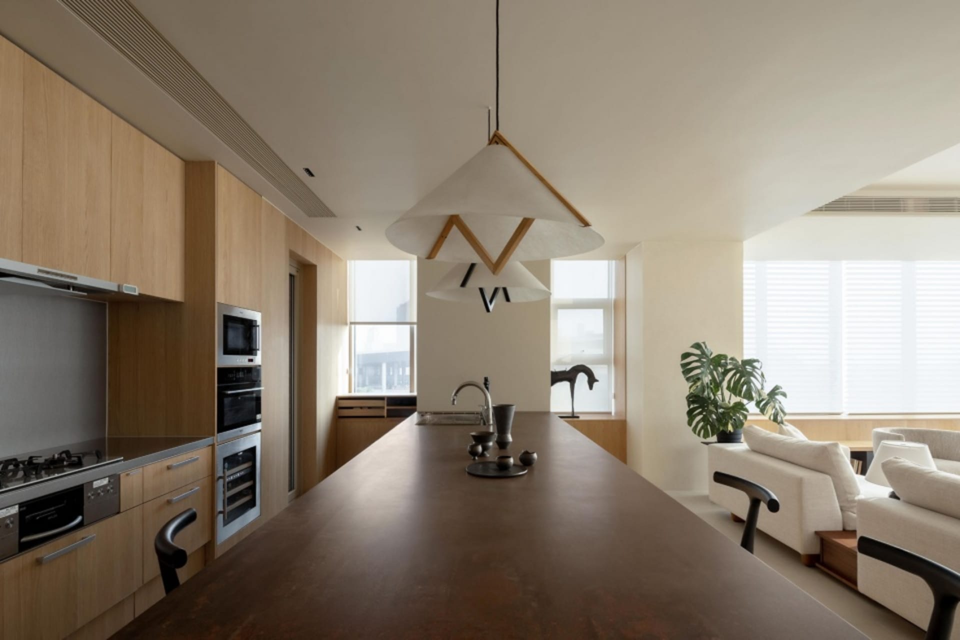 A modern minimalist kitchen with wooden cabinets, white countertops, and black hanging pendant lights.
