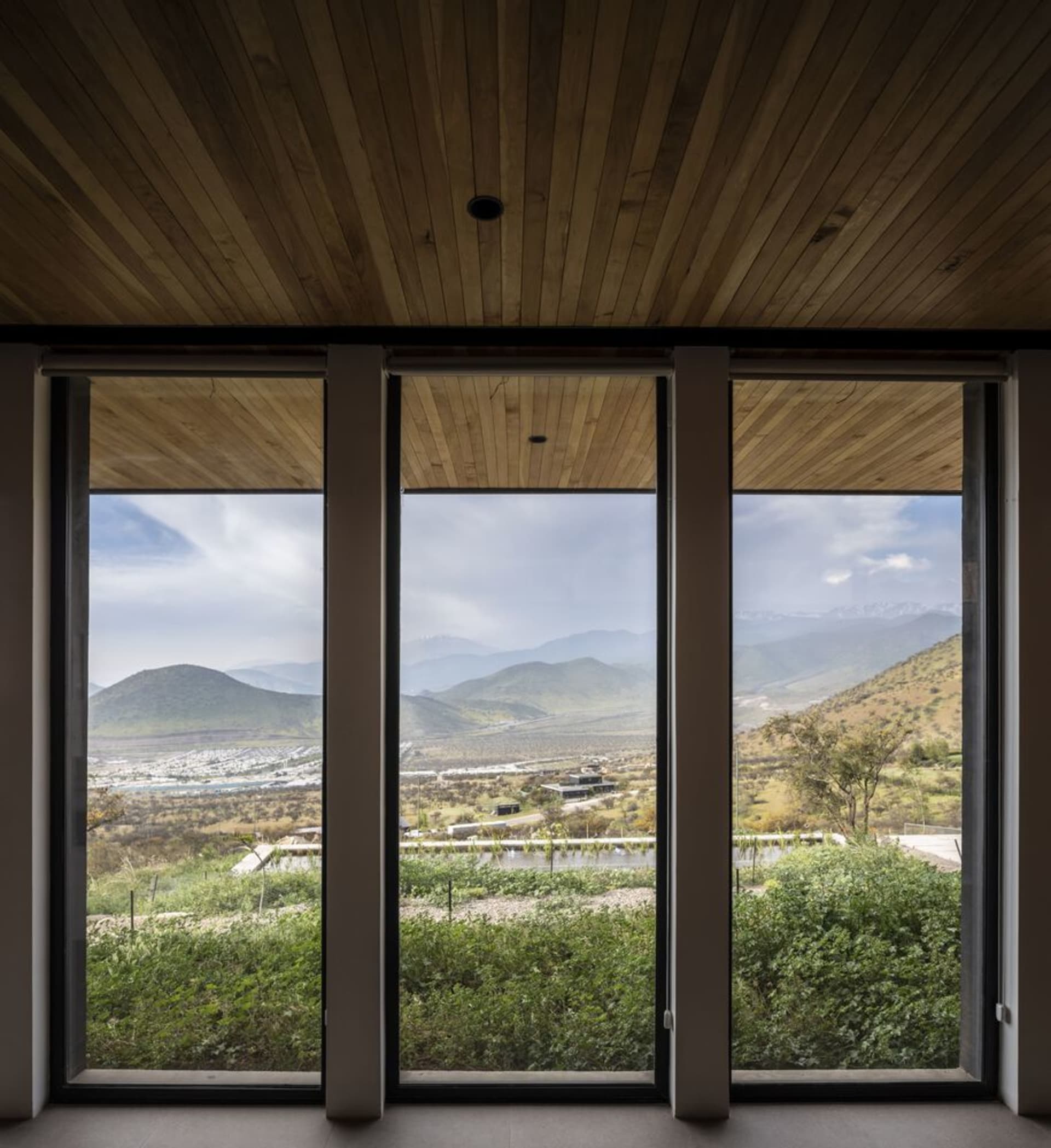 A modern minimalist residential interior featuring large windows with a view of the mountains and lush green landscape.