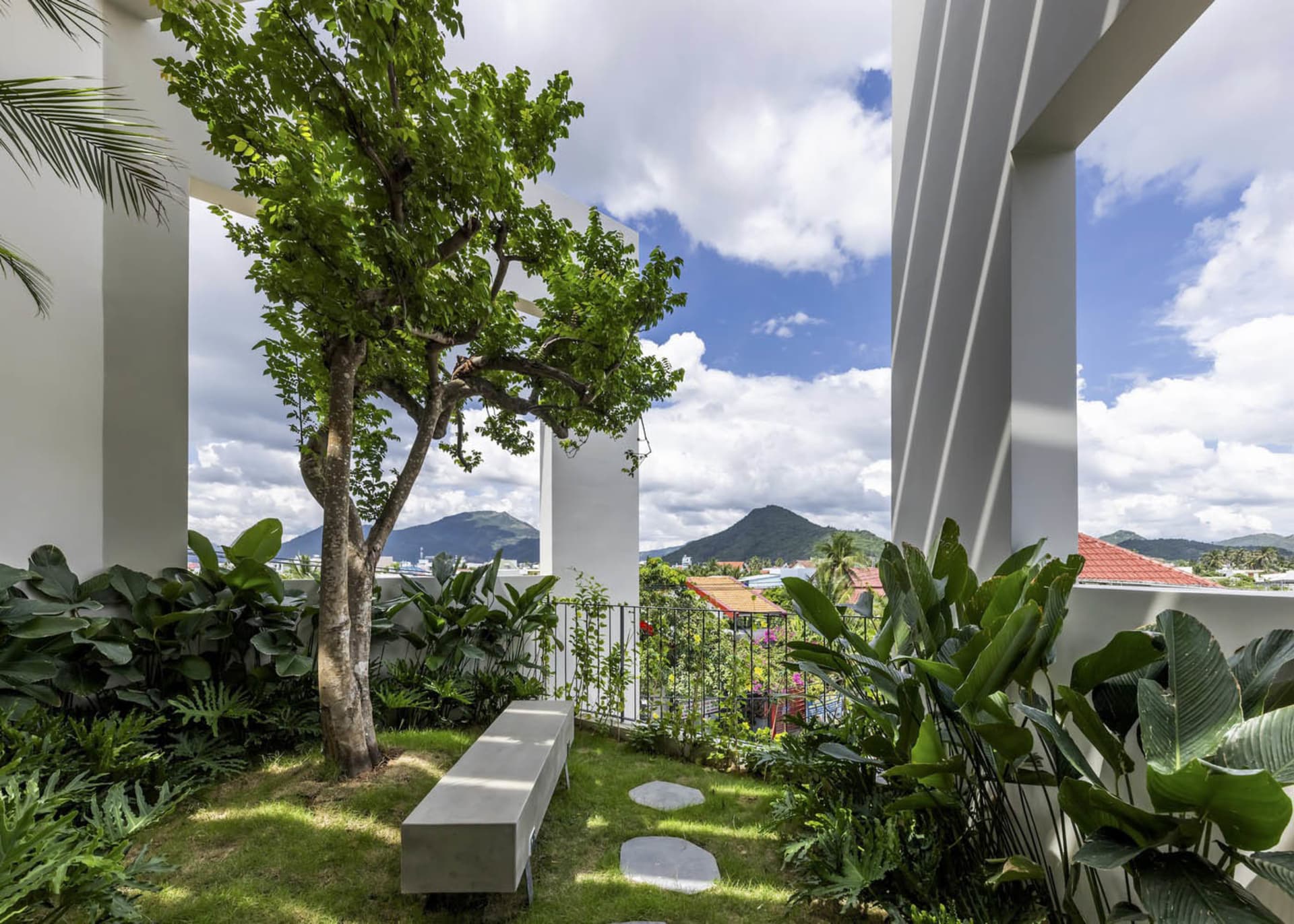 Concrete patio surrounded by lush green plants against a backdrop of mountains under a cloudy sky.
