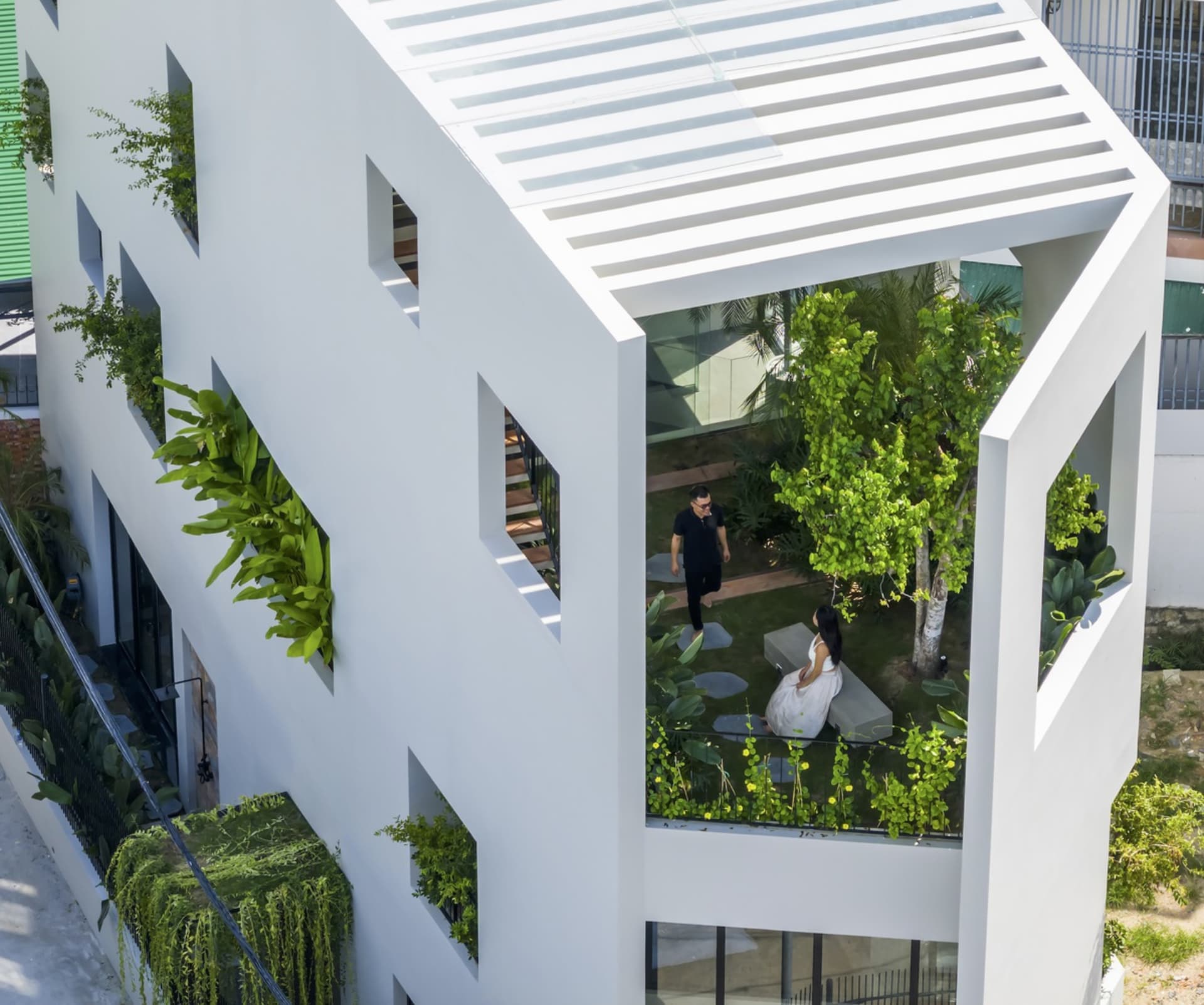 A modern, white building with green plants on the windows and lush greenery surrounding it.