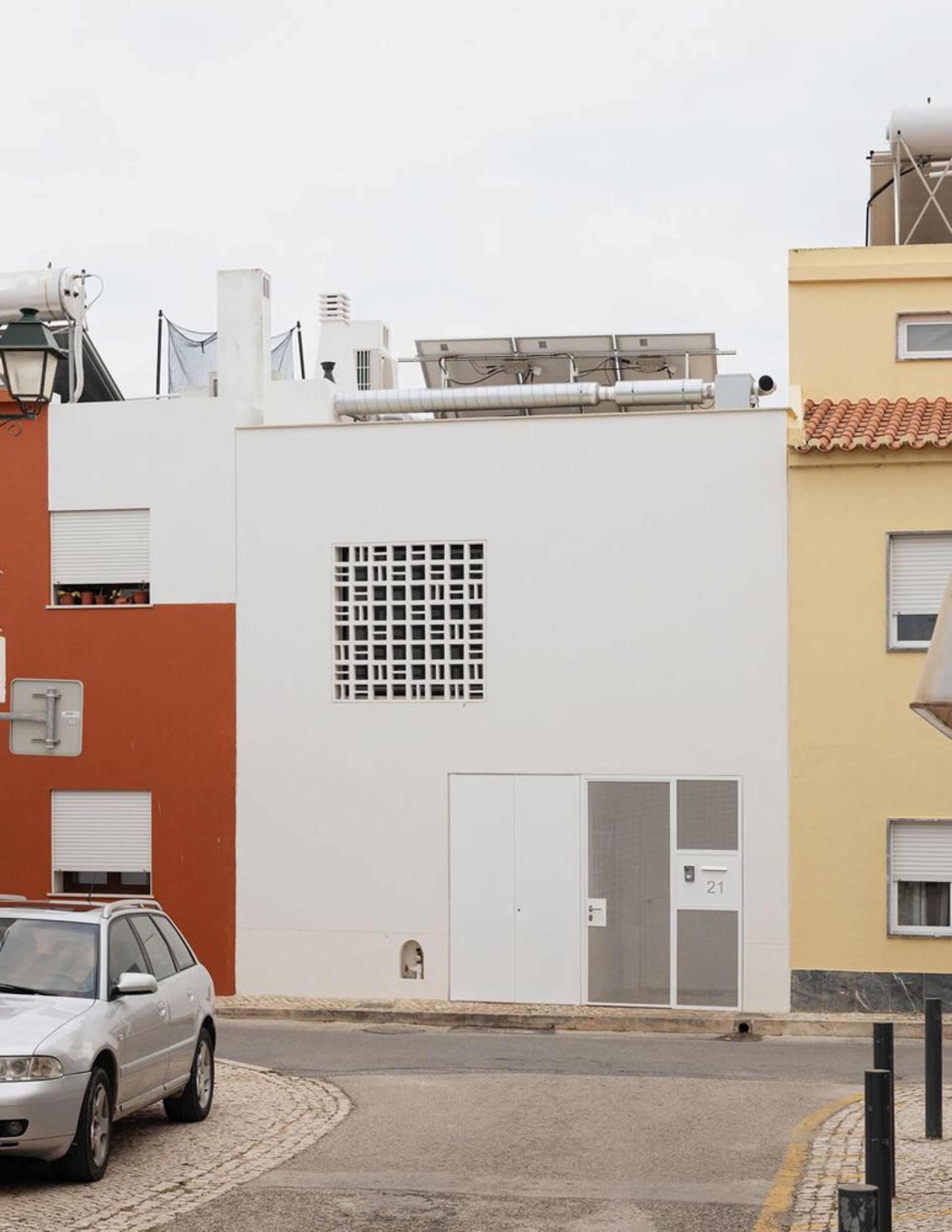 A white-painted residential building facade with a grid-patterned window and metal accents.