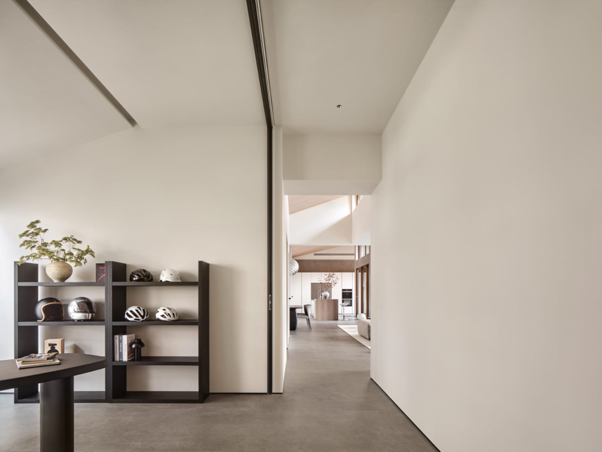 A minimalist home interior featuring a concrete floor and a modern shelving unit displaying decorative items and helmets.