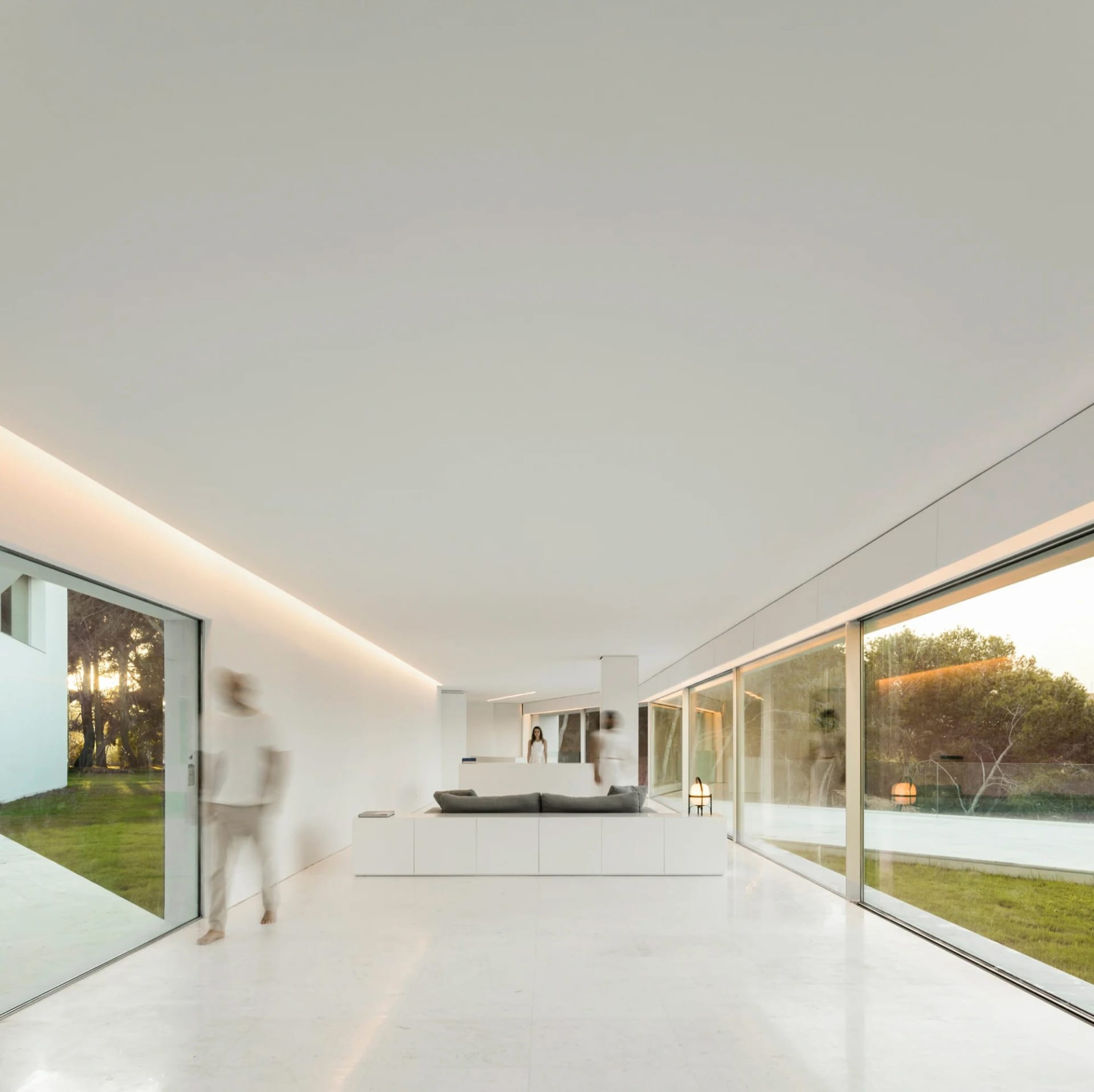 A minimalist living room with concrete walls and floors, featuring a sleek, low-slung sofa and large windows.