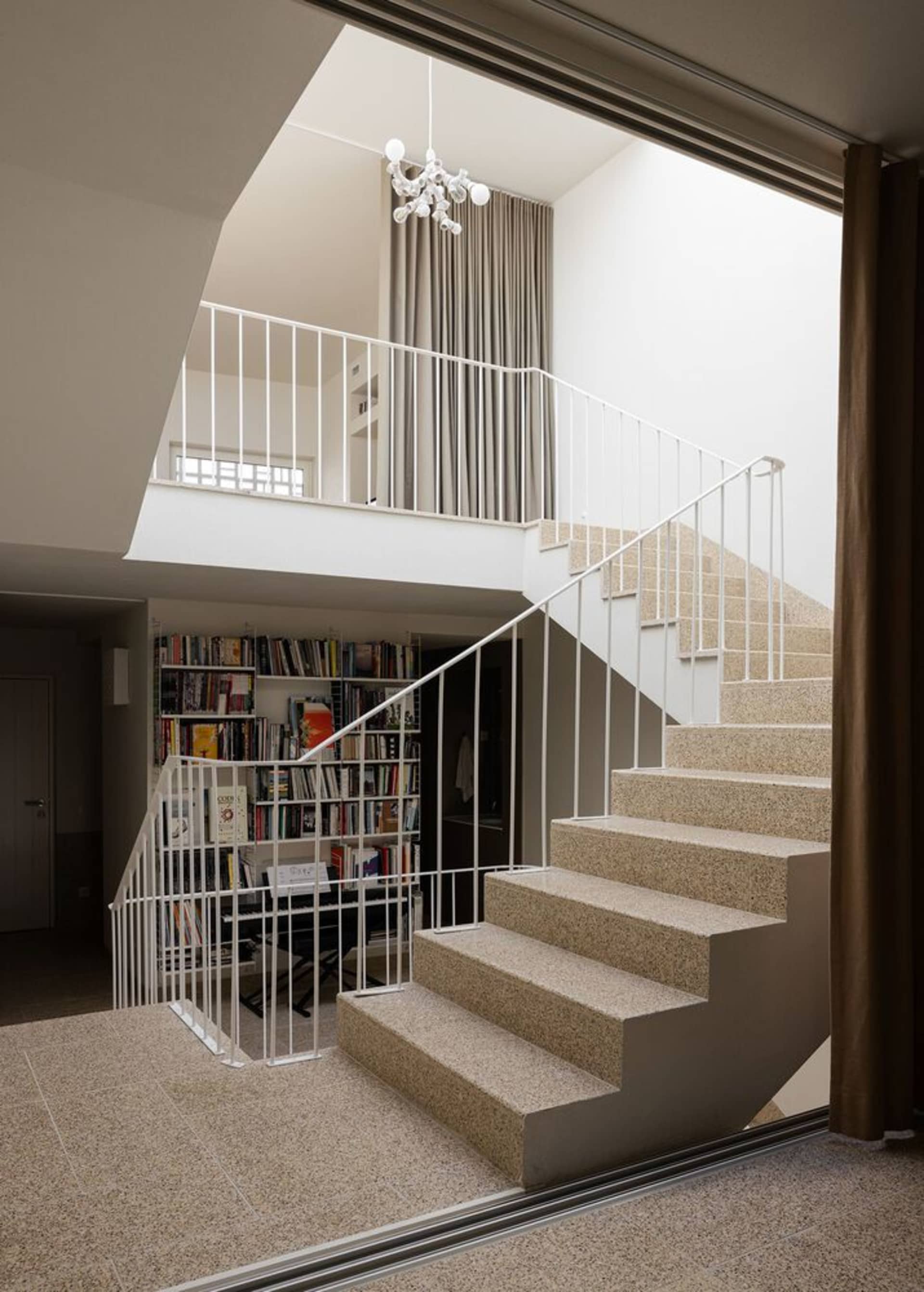 A modern interior space featuring a concrete staircase with metal railings and a bookshelf with books.