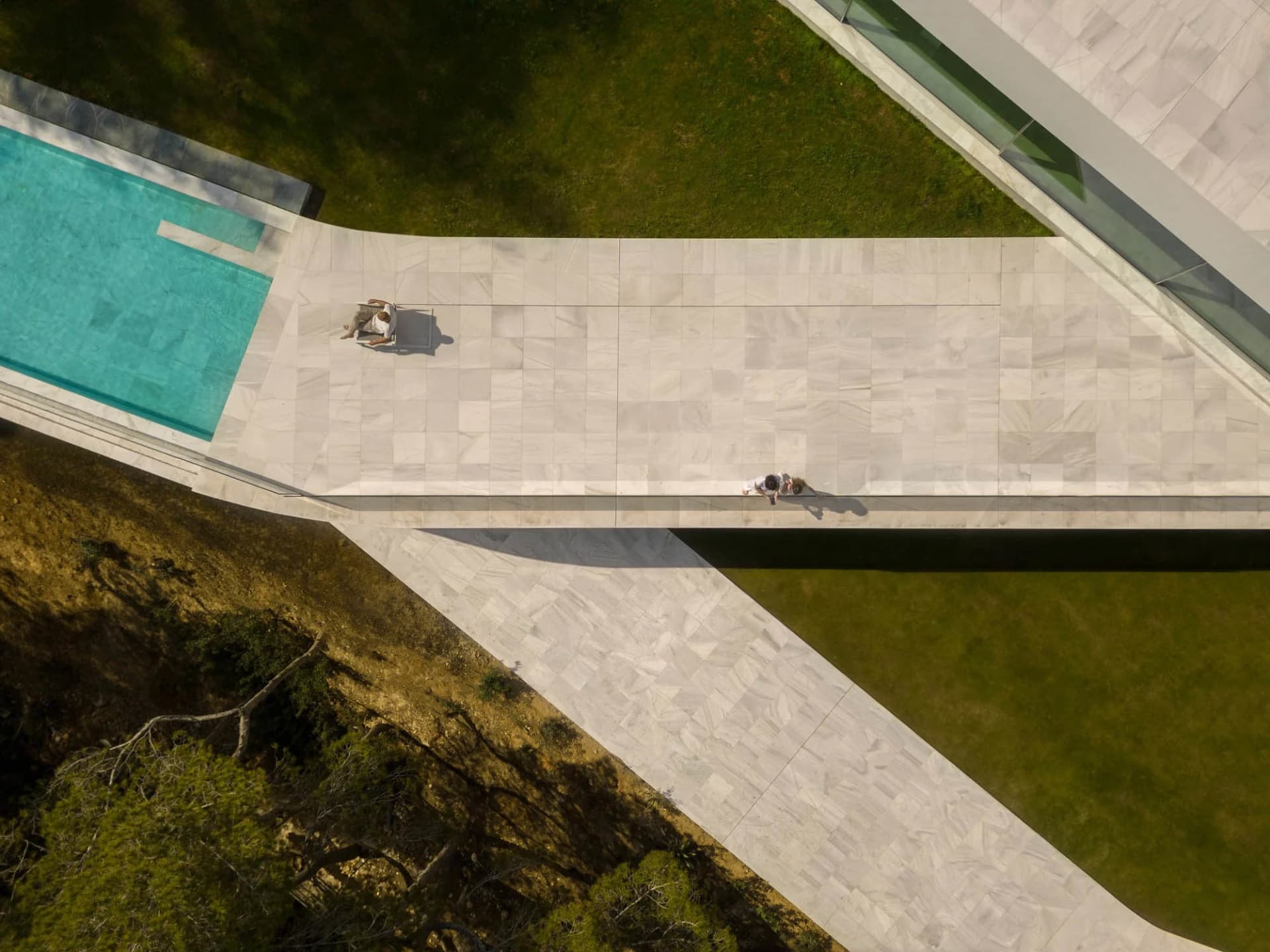 A modern marble pool area with a walkway and greenery.