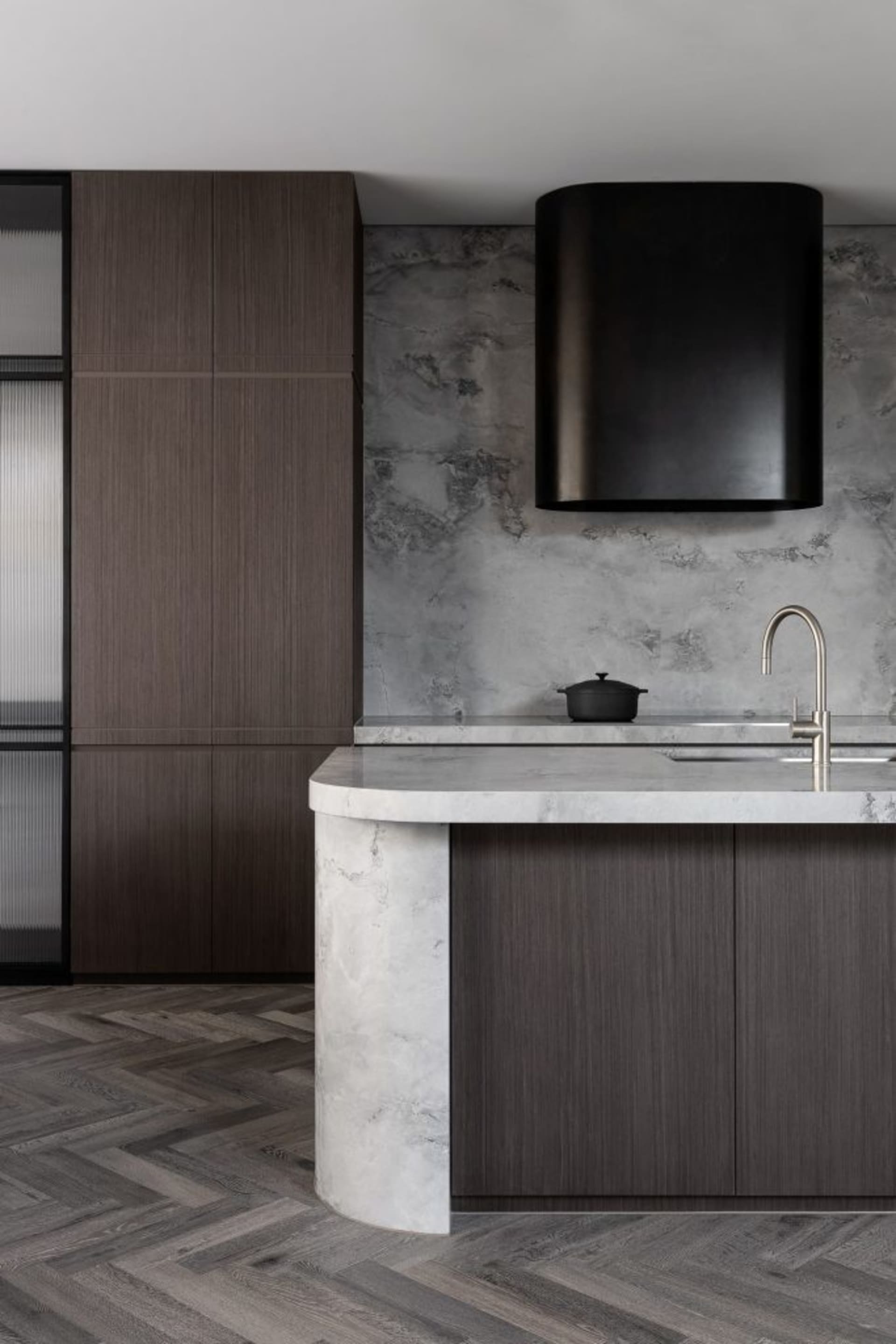 Modern industrial kitchen with a marble countertop, wooden cabinets, and concrete walls.
