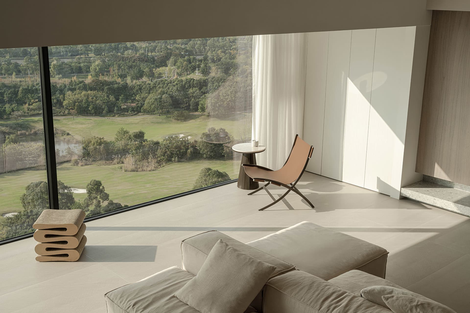 Modern living room featuring minimalist furniture and soft textiles with a view of greenery outside.
