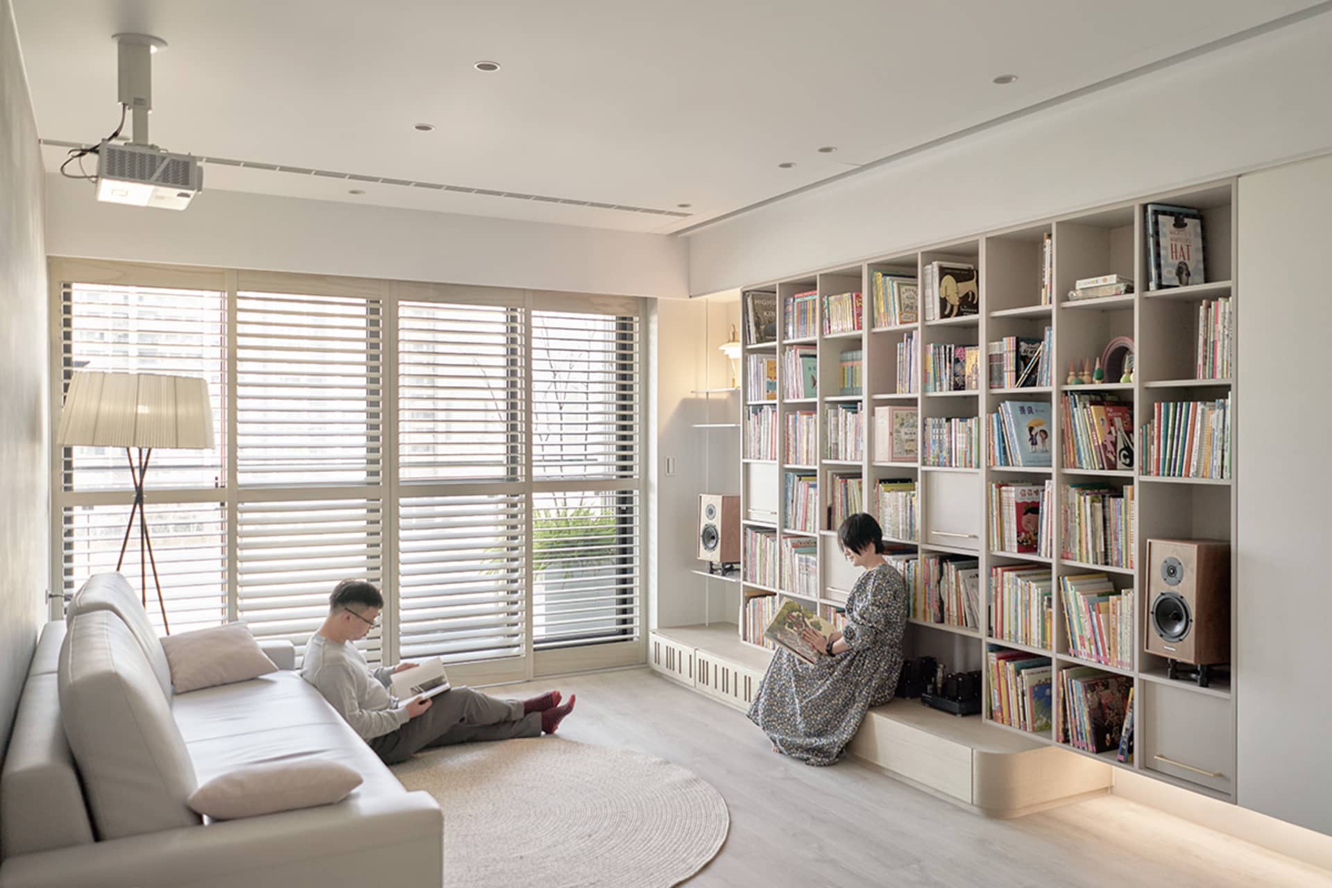 A modern living room with wooden flooring, a white sofa, and a large bookshelf filled with books.