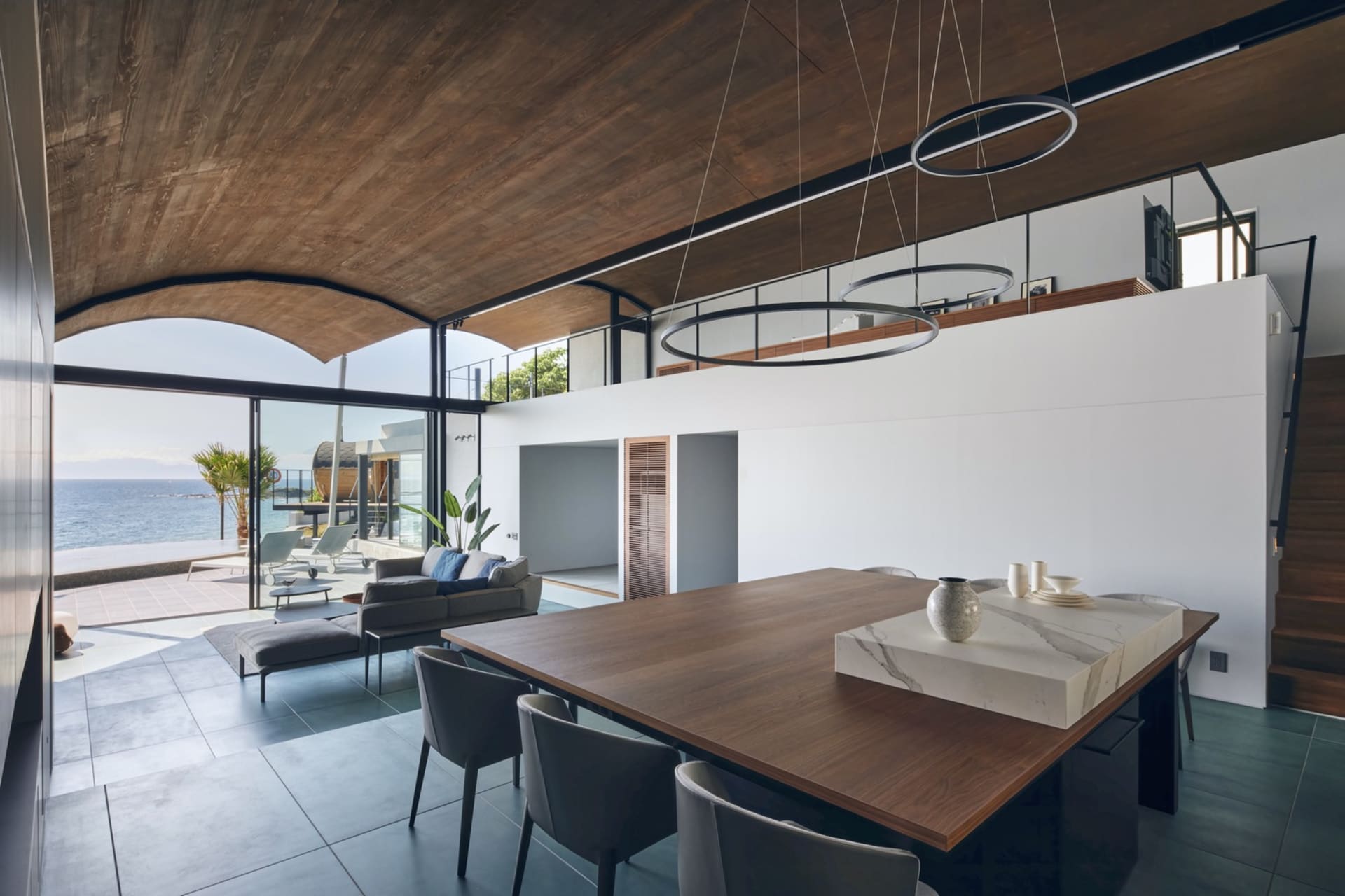 Modern minimalist living room with concrete floor and furniture, large windows with outdoor view of the sea, and minimalist d