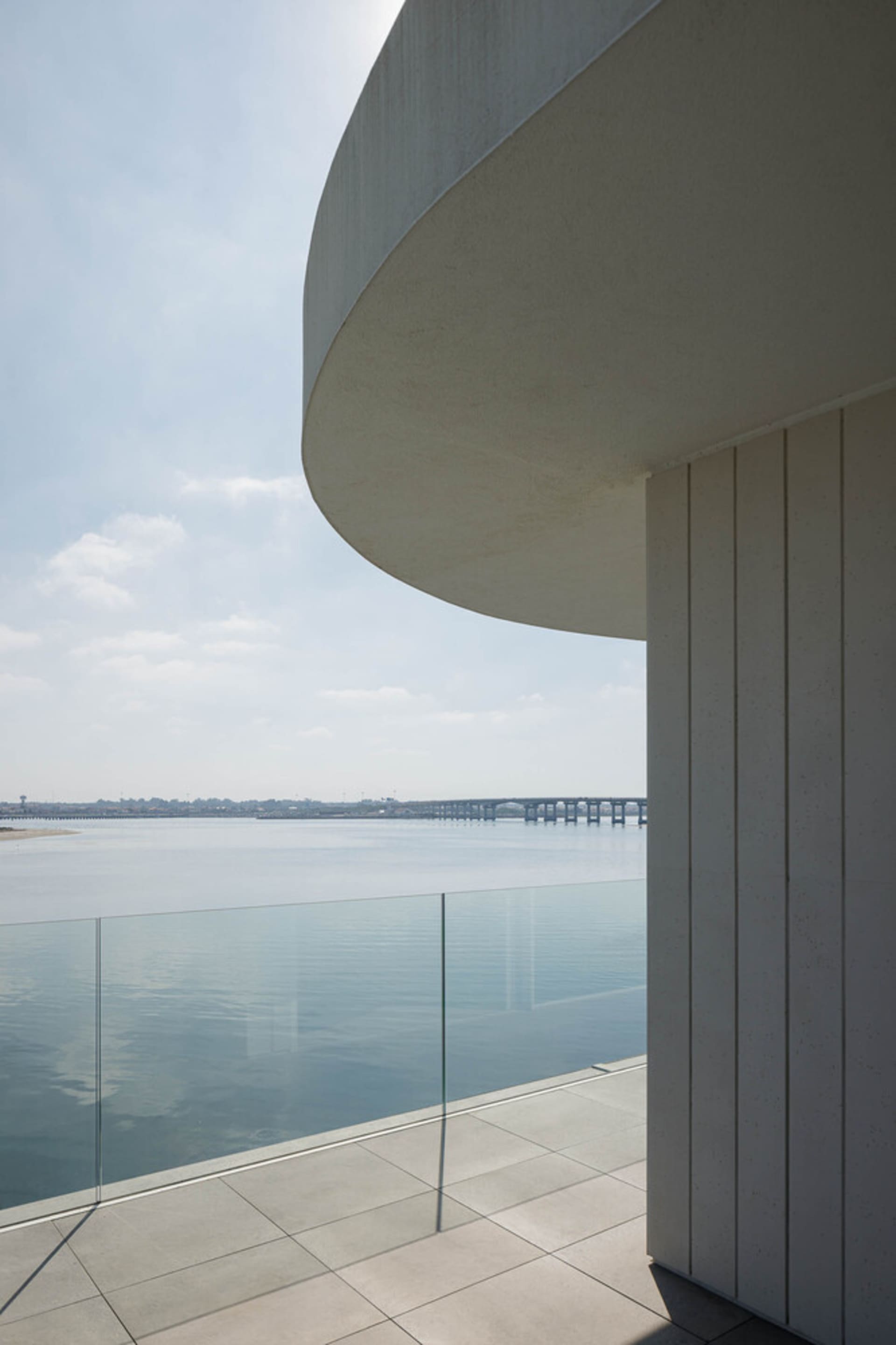 Modern residential balcony featuring concrete flooring and glass balustrade overlooking calm water.