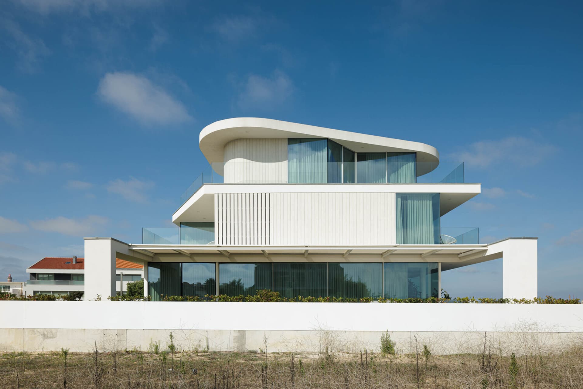 Modern residential house with large glass windows and curved rooftop.