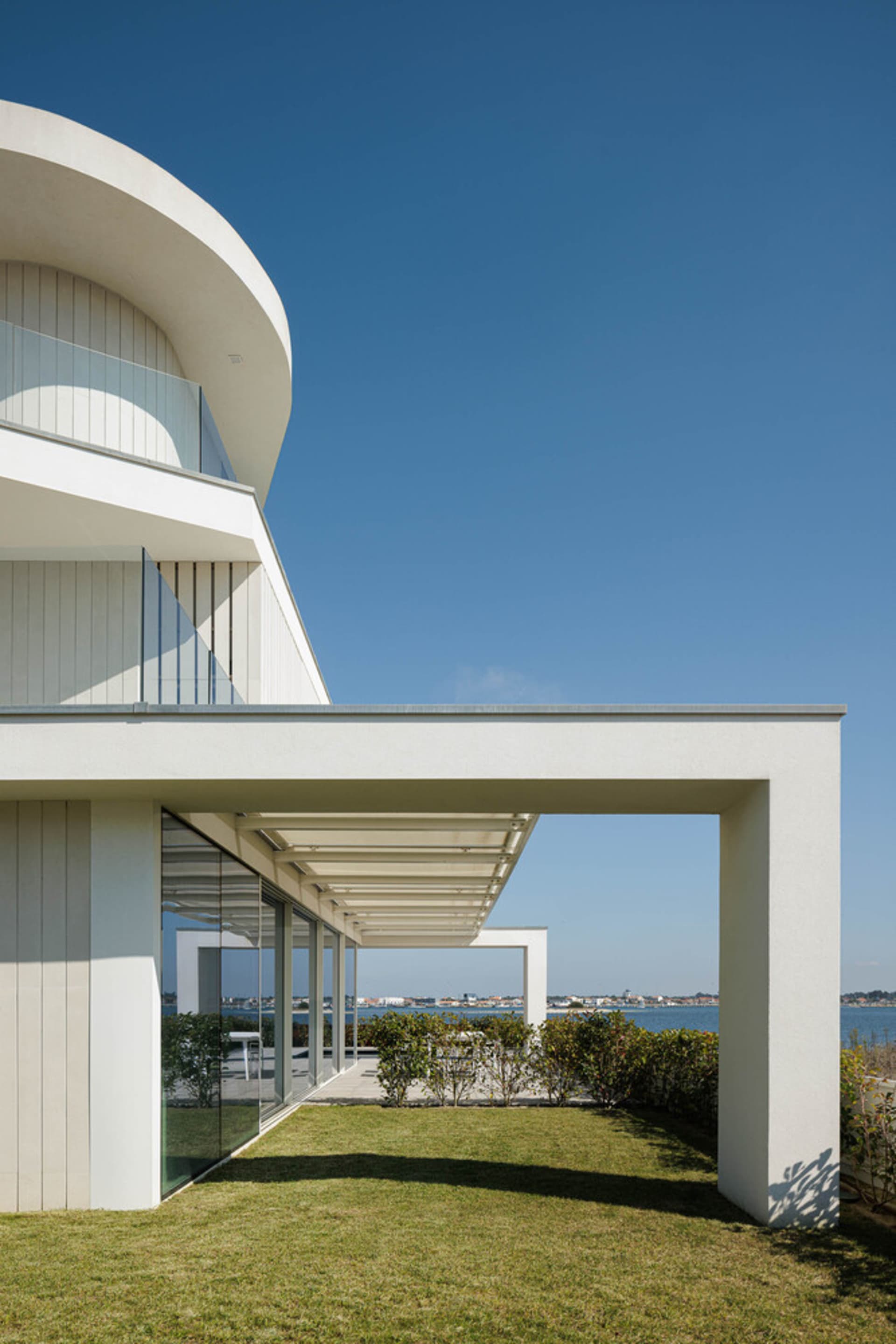 Modern residential exterior with white architectural design, glass walls, metal frame, and green grass