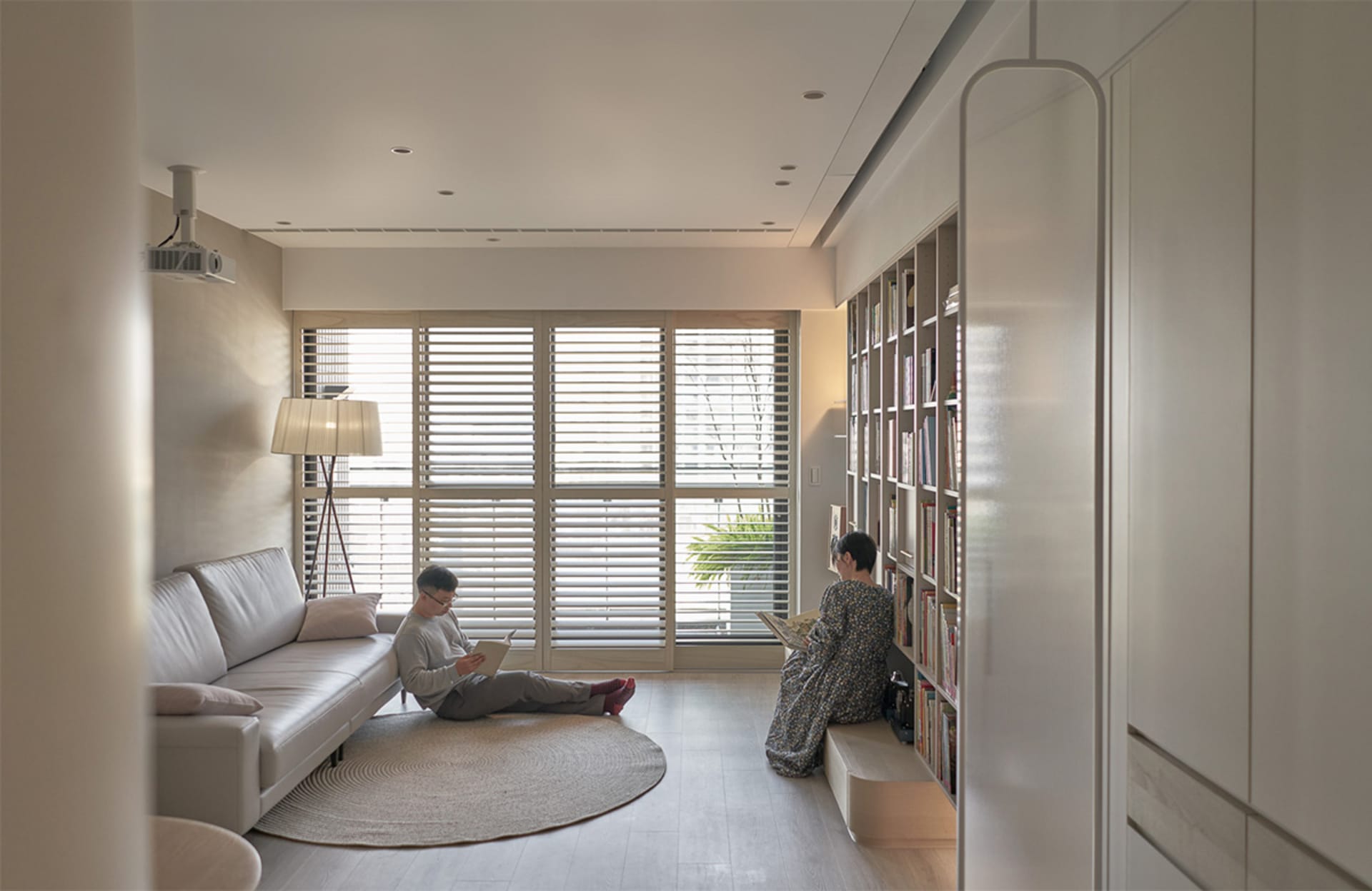 A minimalist living room featuring a white couch, glass shutters, and light wooden flooring.