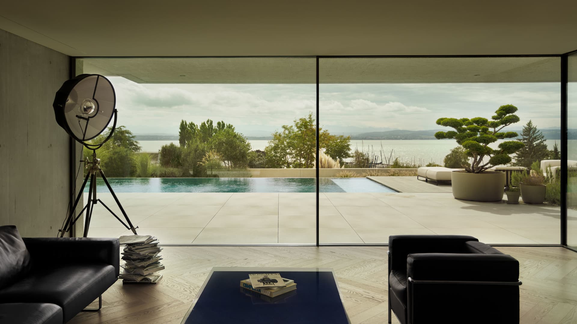 A modern living room featuring a minimalist design with concrete floor and walls, and floor-to-ceiling windows overlooking a