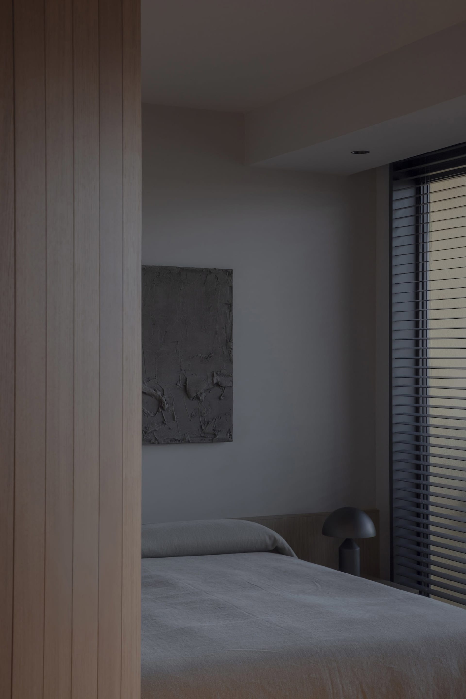 Minimalist bedroom with concrete walls, a simple bed, and a window with blinds.