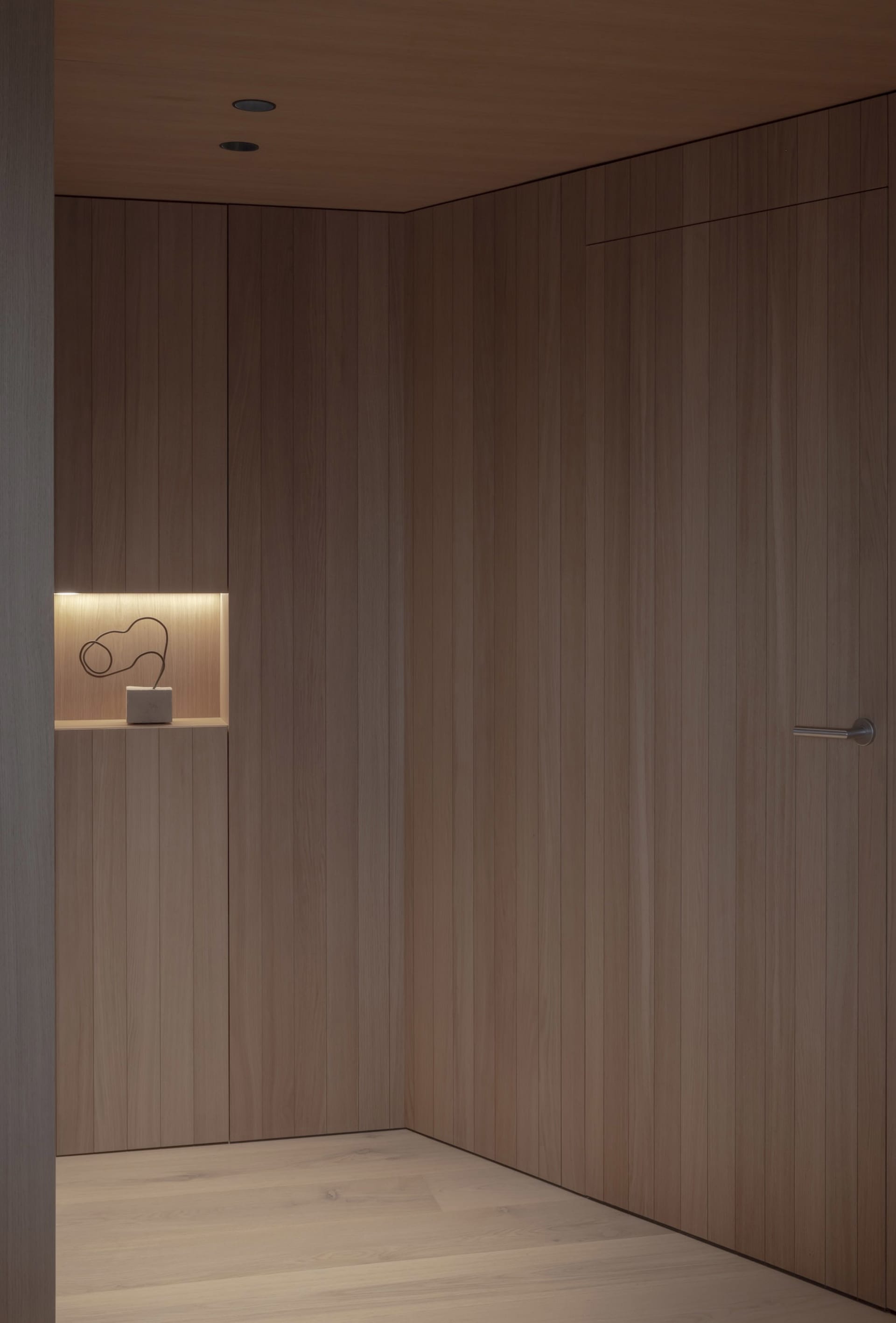 A minimalist closet with wooden panels and a small shelf with a sculptural object.