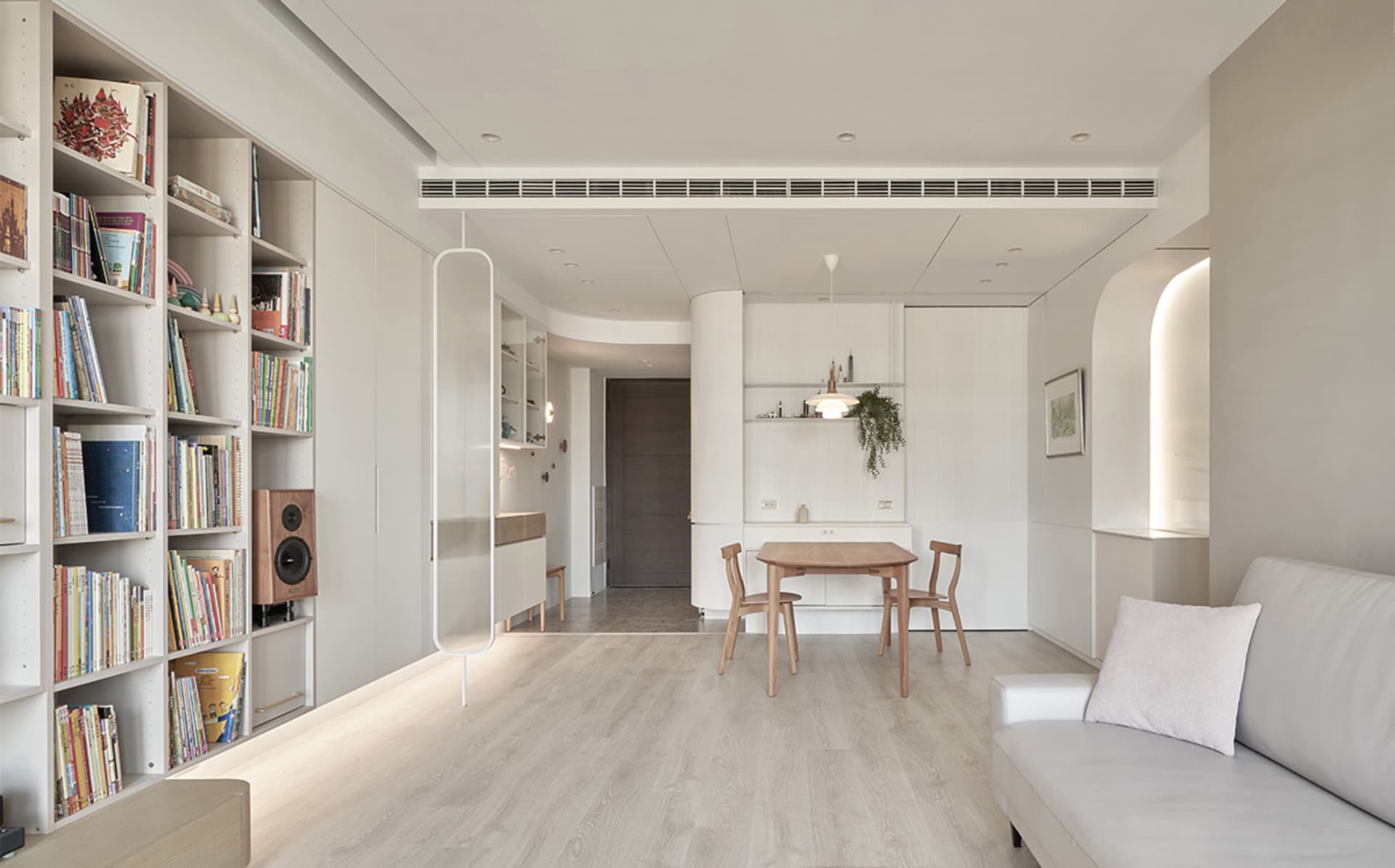 A modern living room with a white couch, wooden dining table, and bookshelf filled with books.